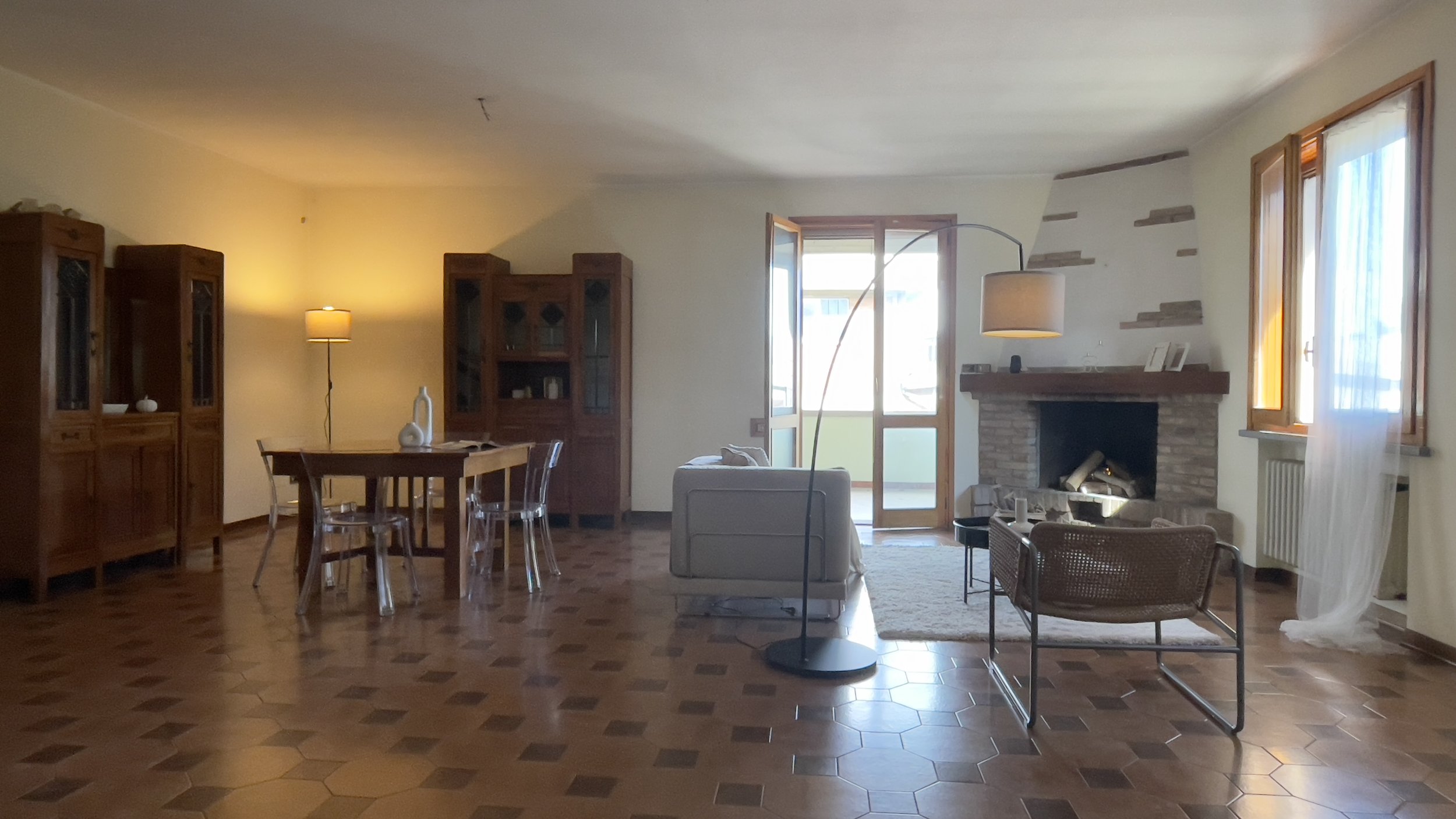 Un soggiorno arredato con mobili in legno, un tavolo con sedie trasparenti, una lampada da terra, un camino in pietra e finestre con tende leggere.