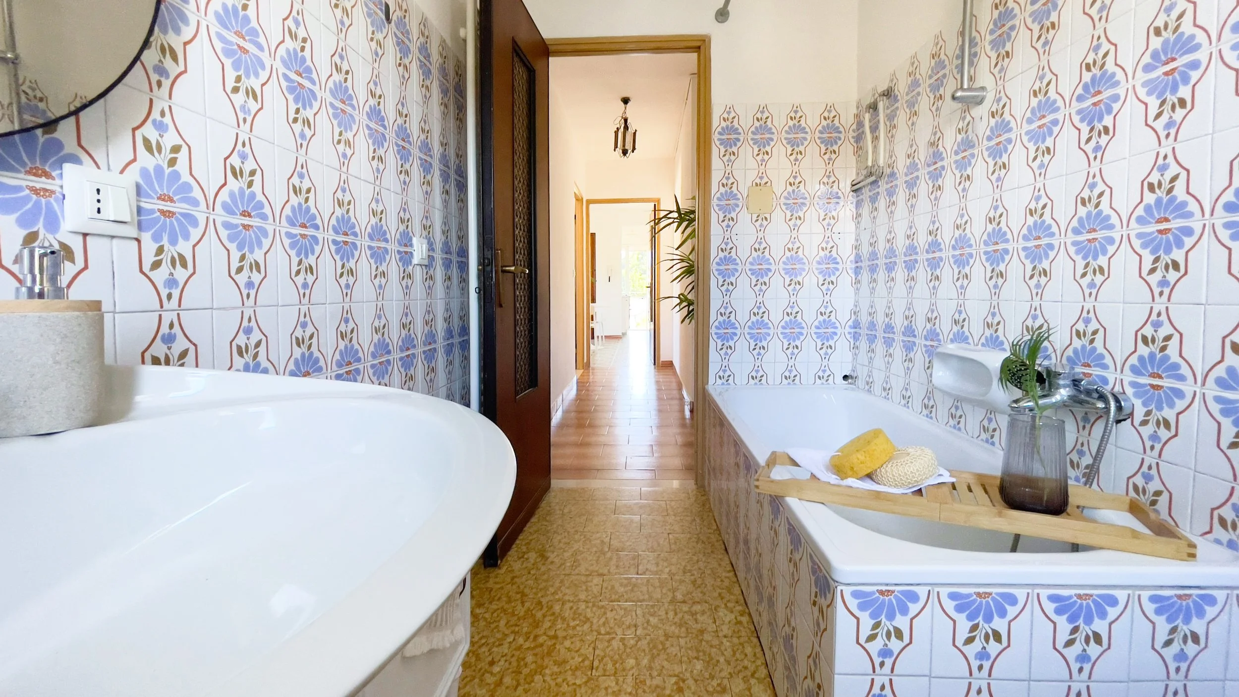 Bagno con piastrelle a fiori blu, vasca da bagno con ripiano in legno, specchio e lavabo bianco.