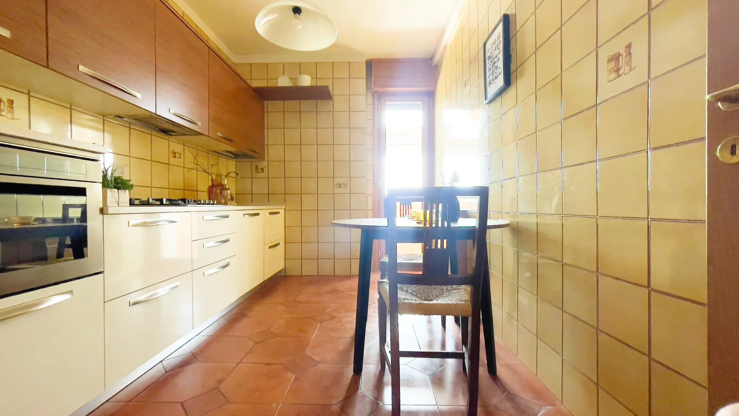 Cucina con mobili moderni, forno, fornelli a gas, tavolo rotondo e sedie di legno, piastrelle beige e lampadario.