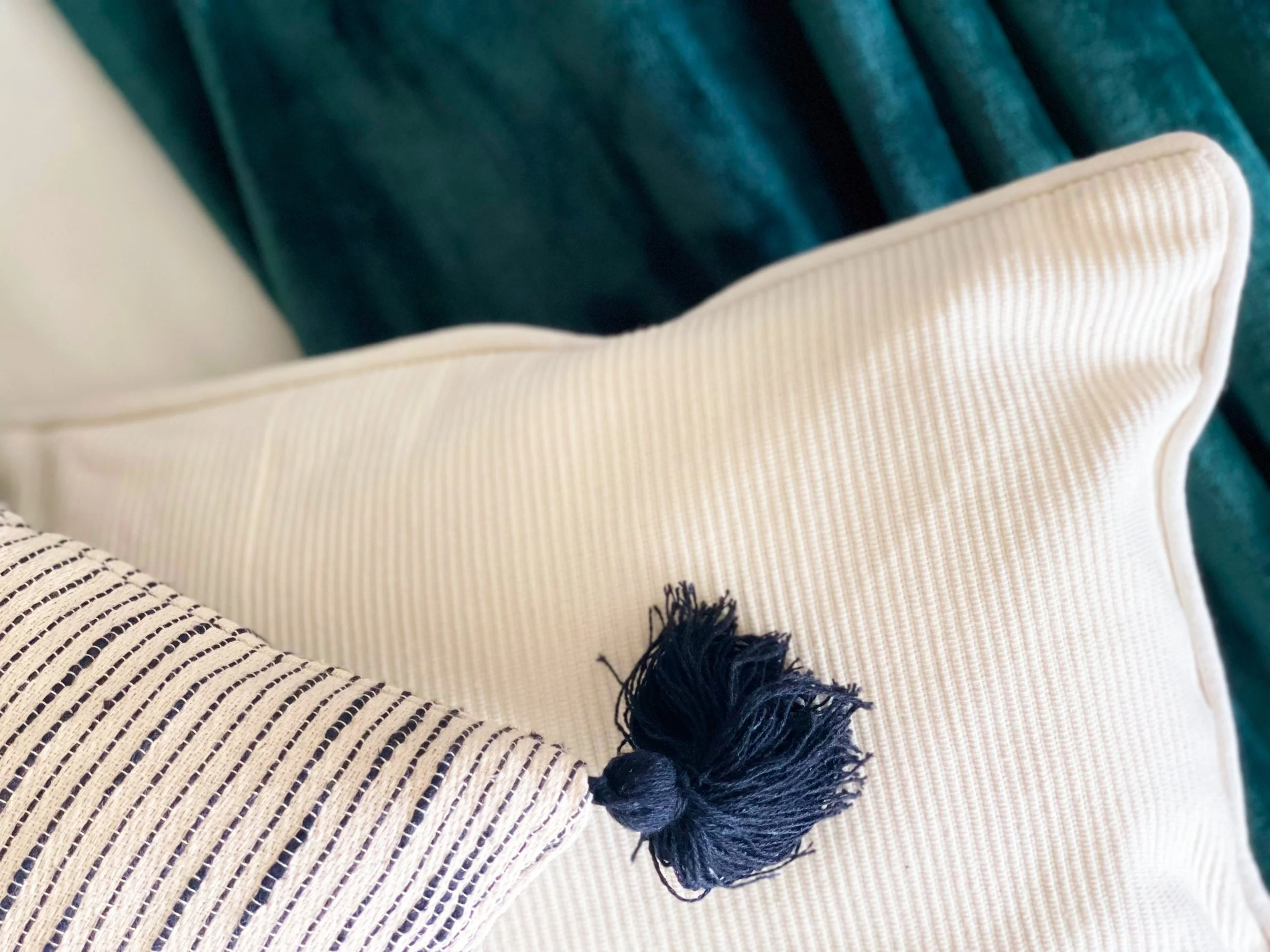 Cuscini decorativi su sfondo verde scuro, uno con nappa nera.