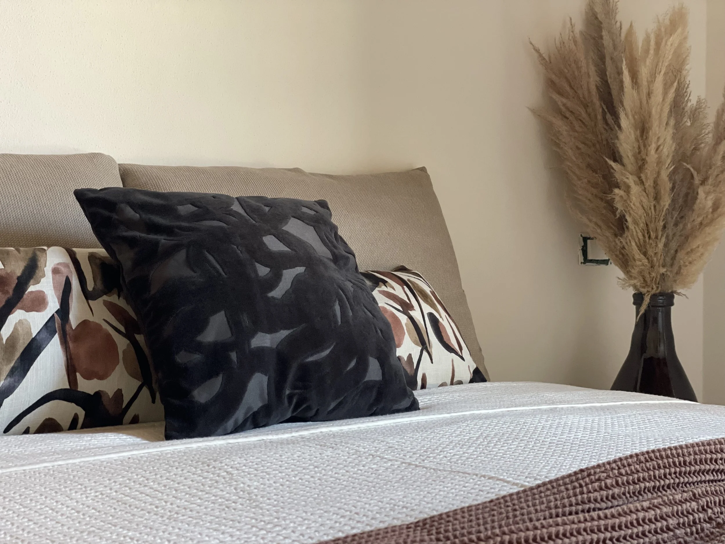 Letto con cuscini decorativi e pianta di pampas in vaso.
