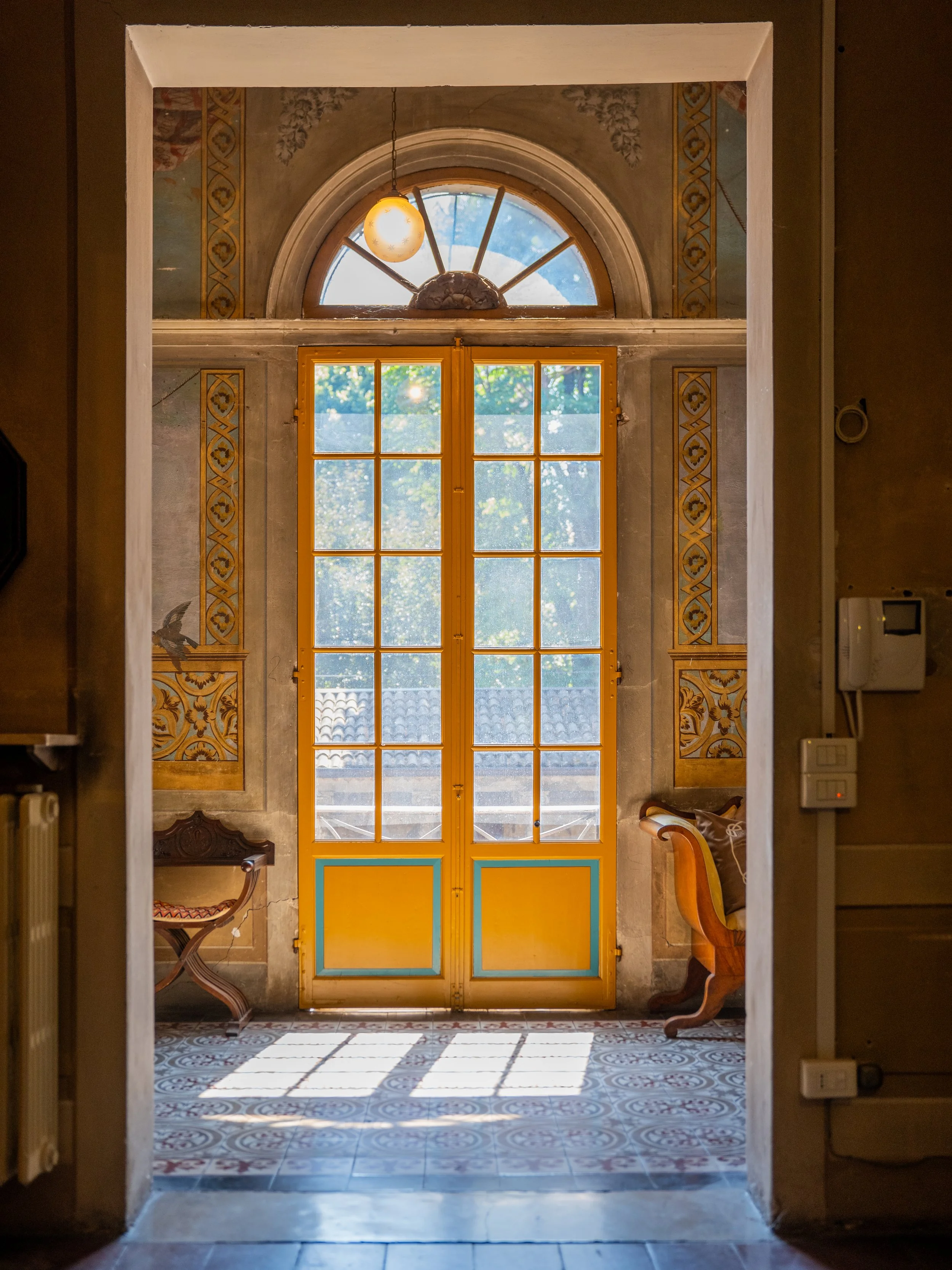 Porta d'ingresso con vetrate colorate e disegni decorativi, in un ambiente interno con pavimento decorato e arredi antichi.