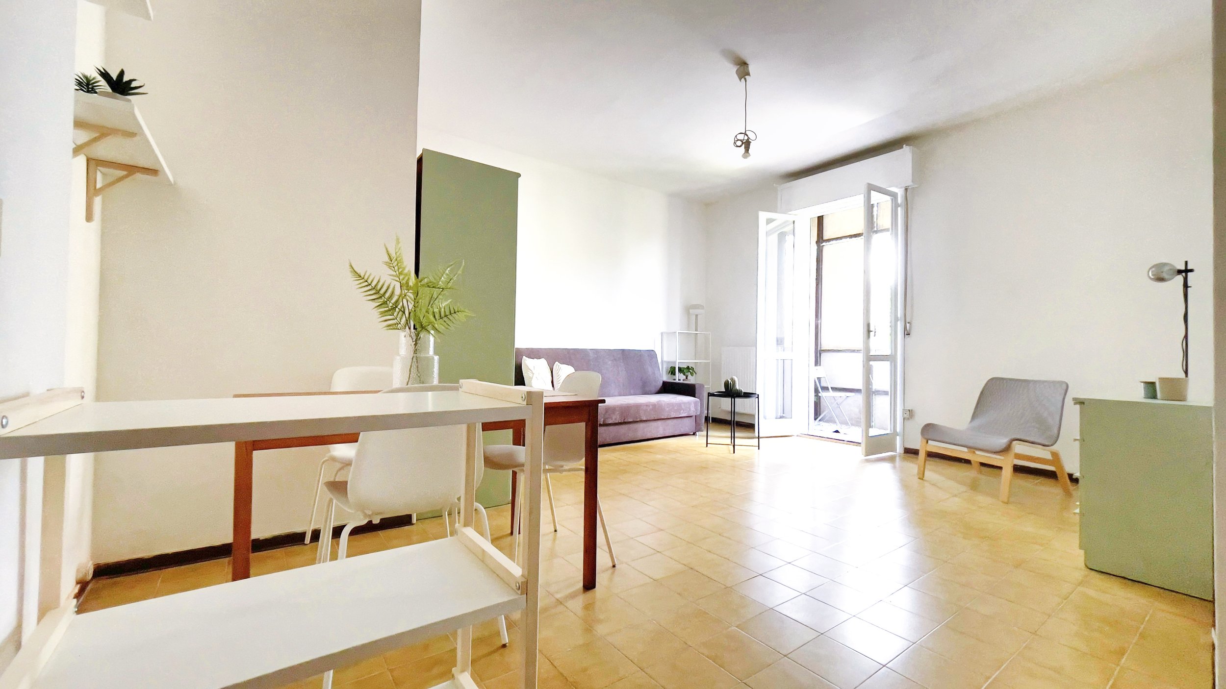 Soggiorno luminoso con tavolo, sedie bianche, divano grigio, poltrona e mobili moderni; porta finestra aperta su balcone.