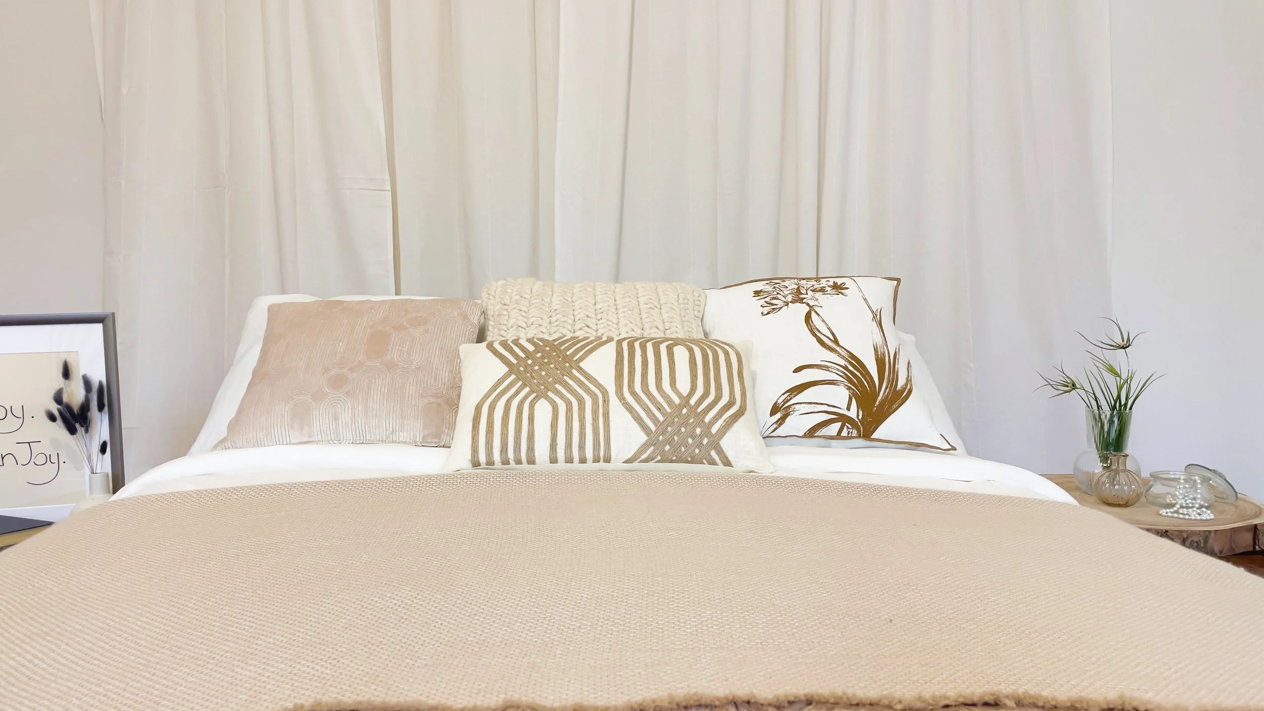 Camera da letto minimalista con cuscini decorativi e coperta beige.