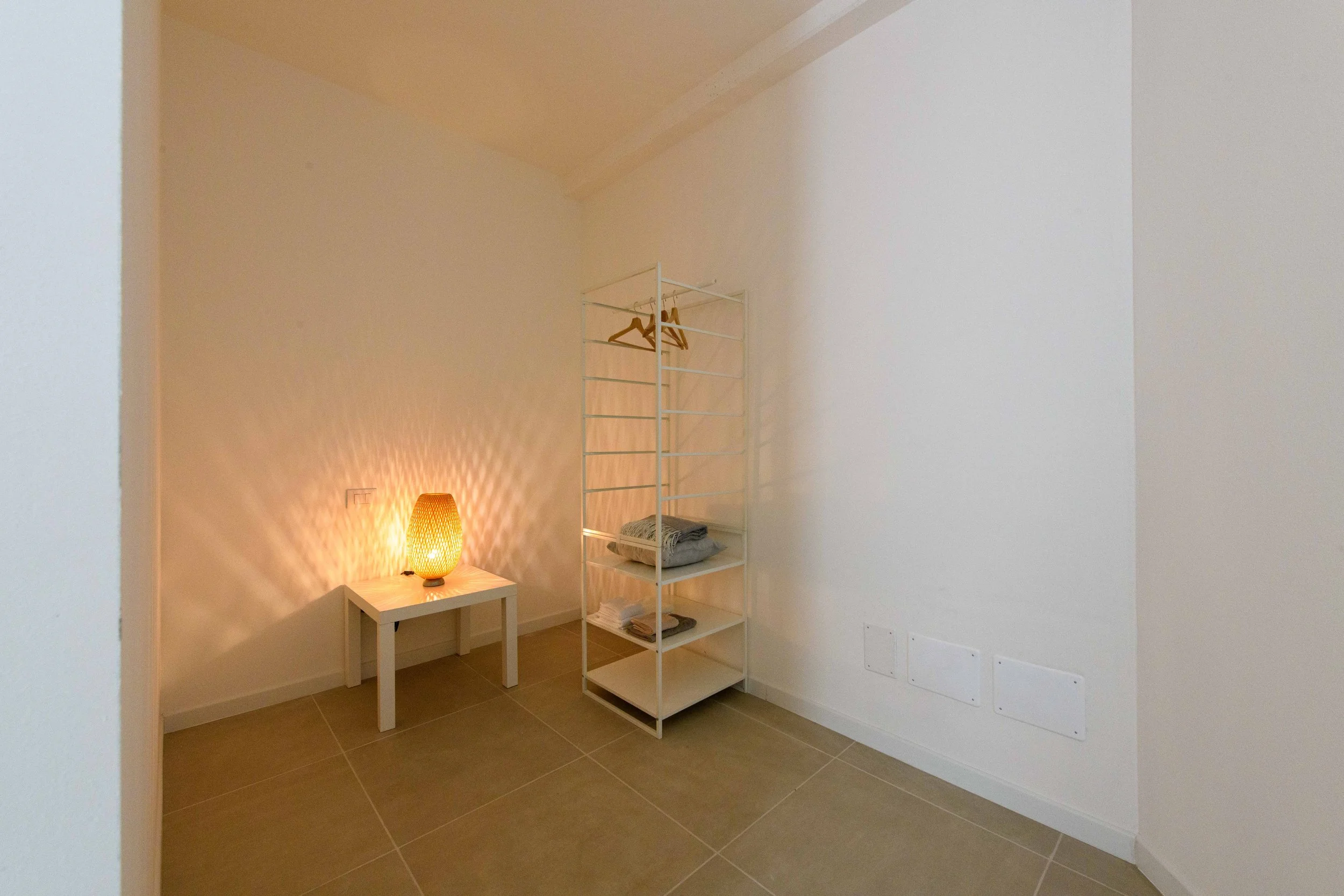 Interno di una stanza con lampada su un tavolo e scaffale angolare bianco.
