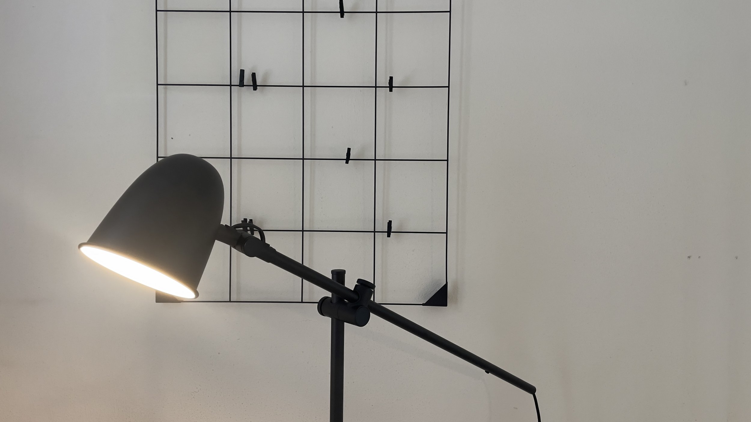 Lampada da tavolo nera accesa vicino a una griglia metallica decorativa fissata al muro.