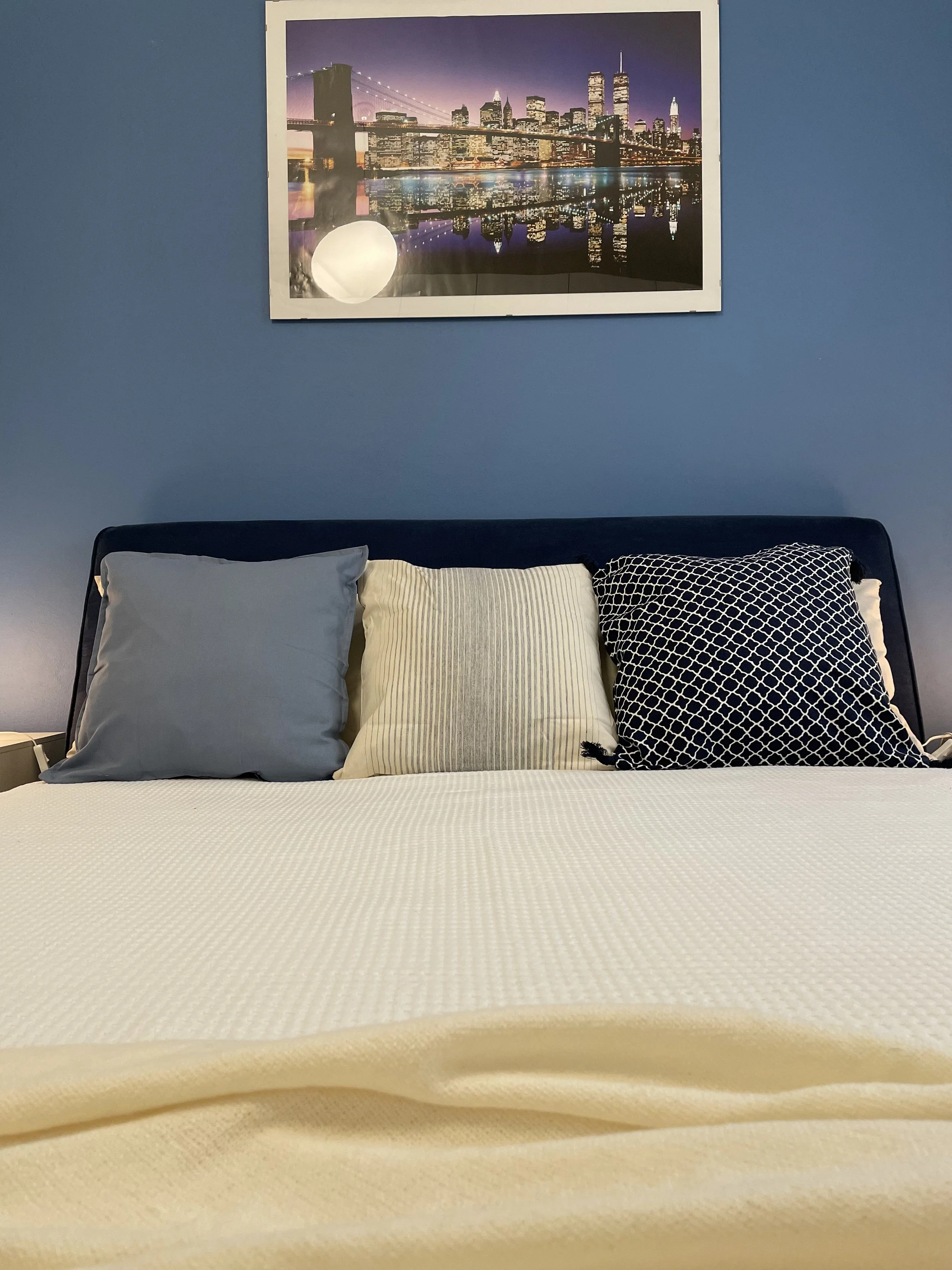 Letto con cuscini e quadro di skyline su parete blu.