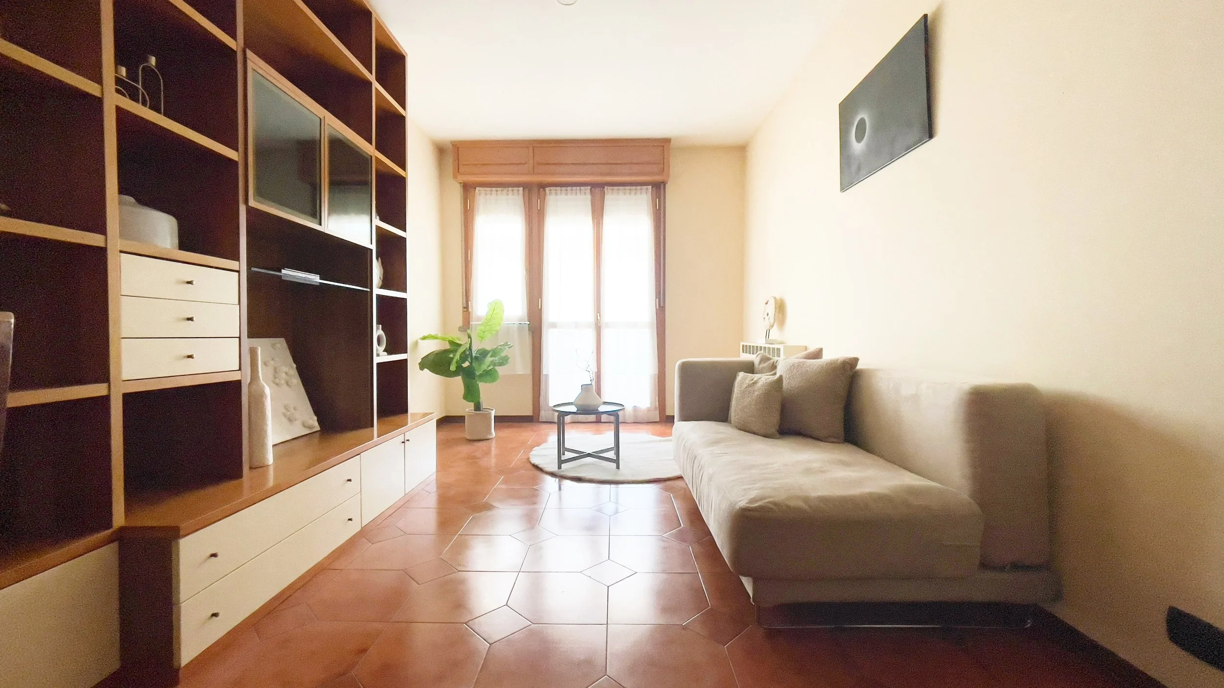 Soggiorno con divano beige, mobili moderni a muro, pianta d'appartamento e tavolino rotondo.