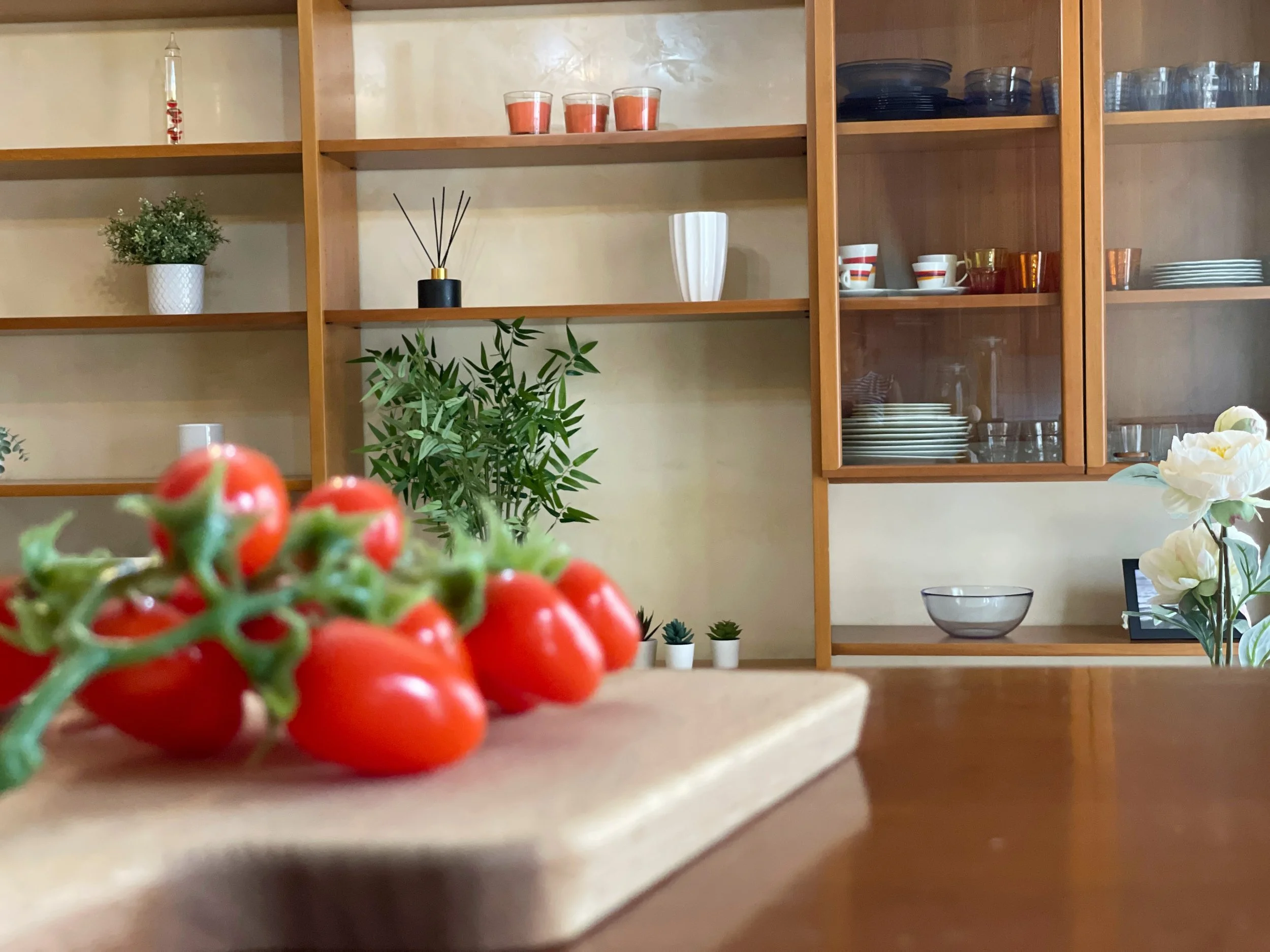 Pomodori su un tagliere di legno in una cucina con scaffali e piante.