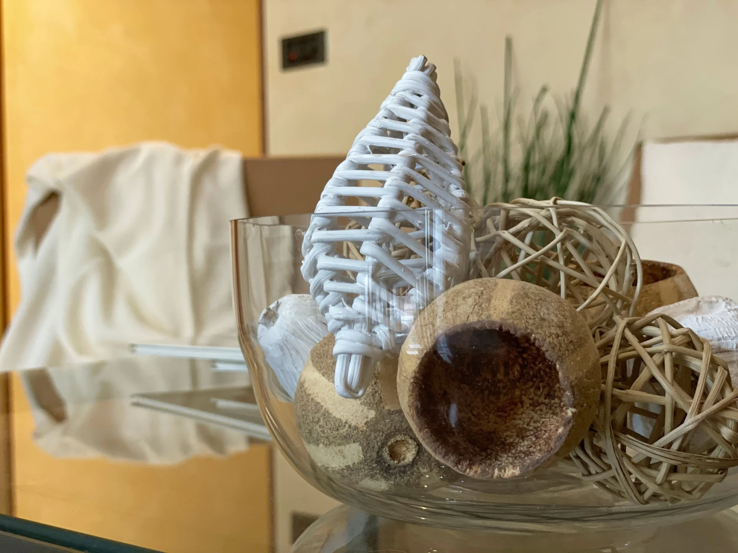 Ciotola decorativa di vetro con sfere di vimini e oggetti naturali, su un tavolo in un soggiorno.