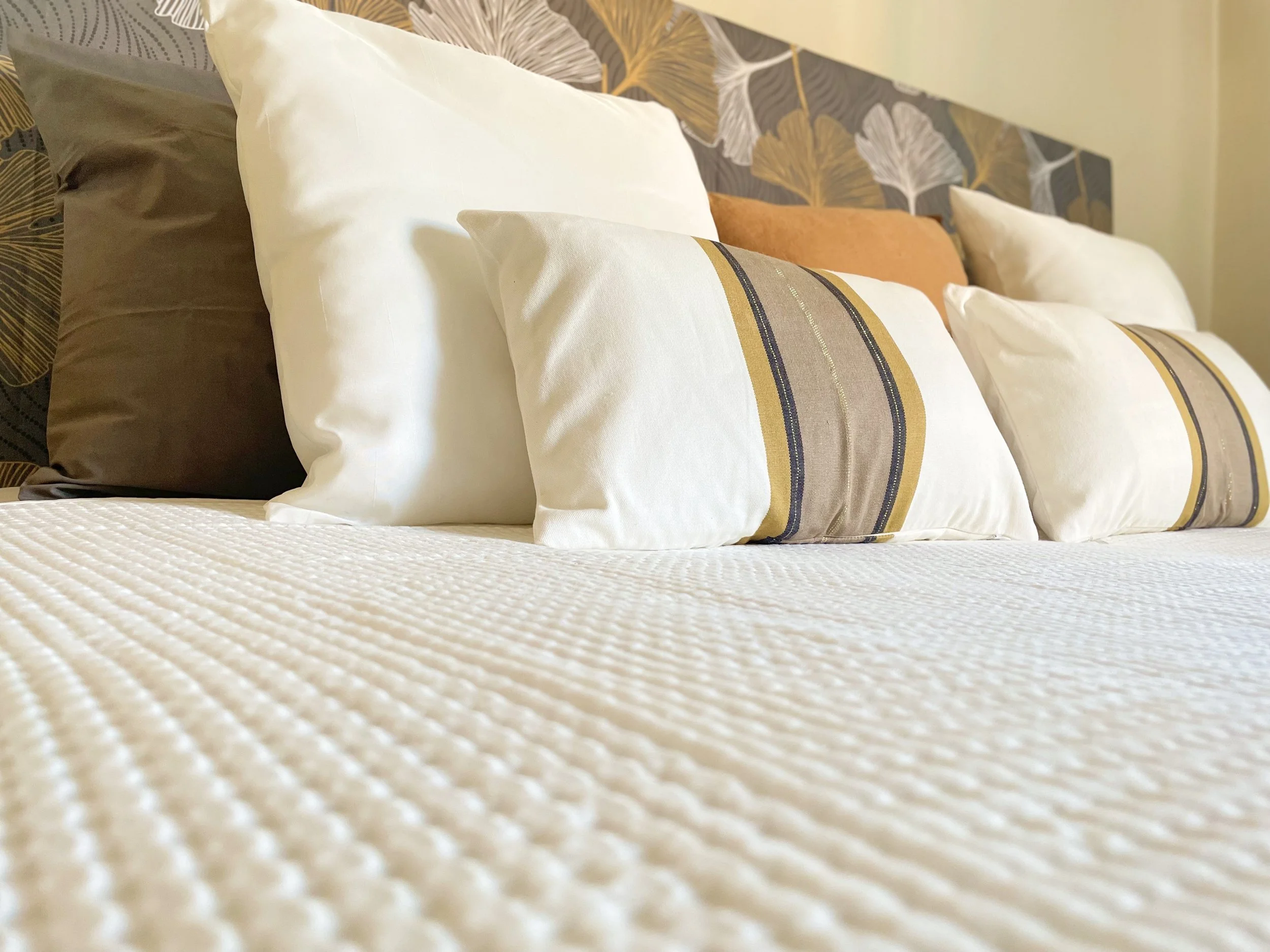 Letto con lenzuola bianche e cuscini decorativi a strisce su testiera con motivo floreale.