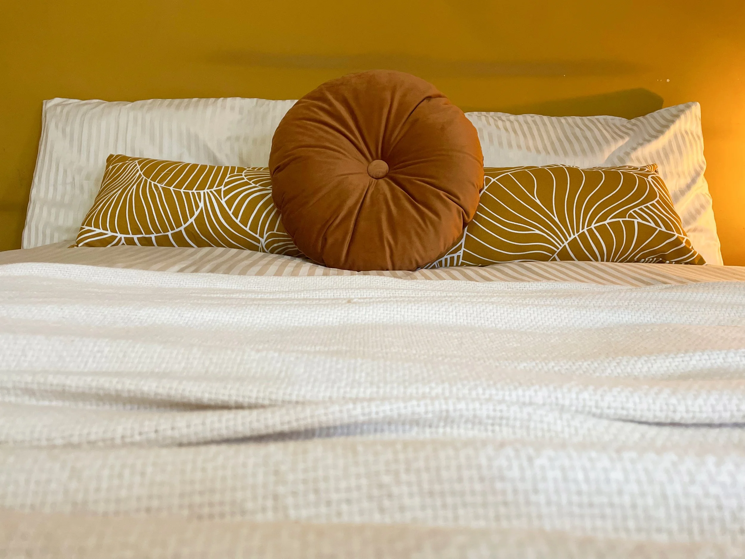 Letto con cuscini decorativi su uno sfondo giallo ocra.