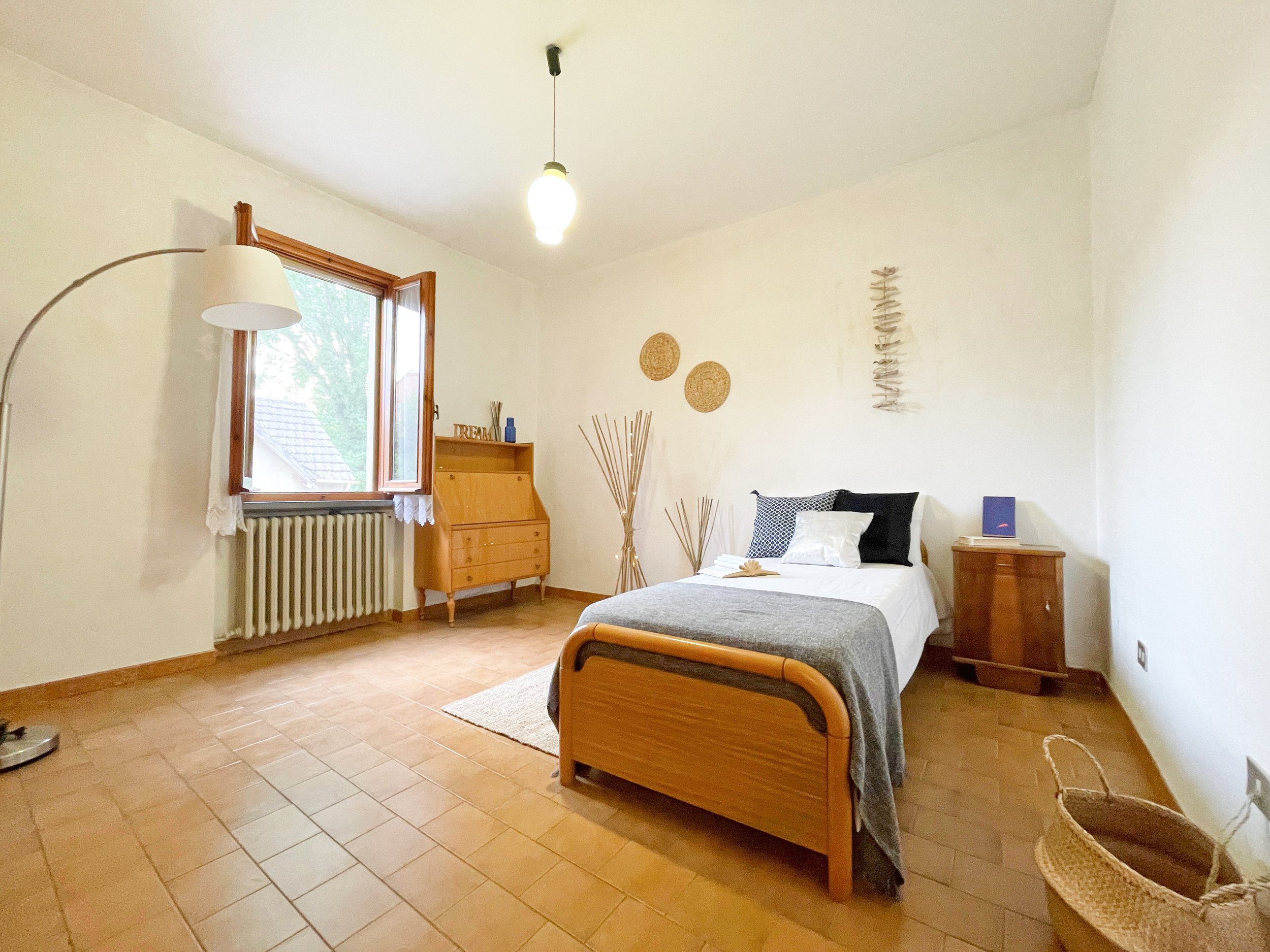 Camera da letto con letto singolo, lampada ad arco, scrivania in legno, e decorazioni minimaliste sulle pareti.