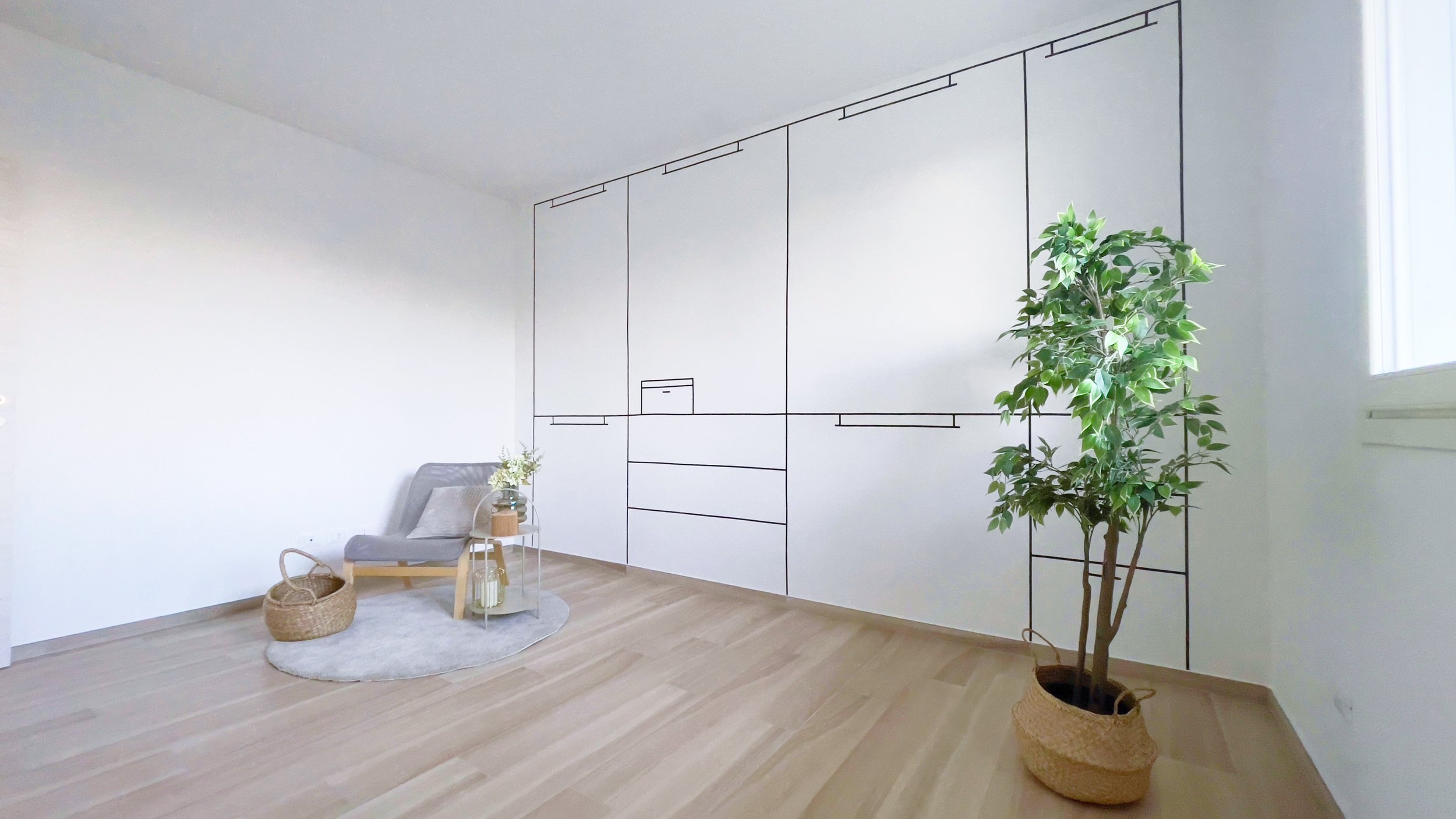 Stanza minimalista con pareti bianche, sedia grigia, piccolo tavolino con vaso di fiori, tappeto rotondo grigio, cestino di vimini e pianta in vaso in angolo.