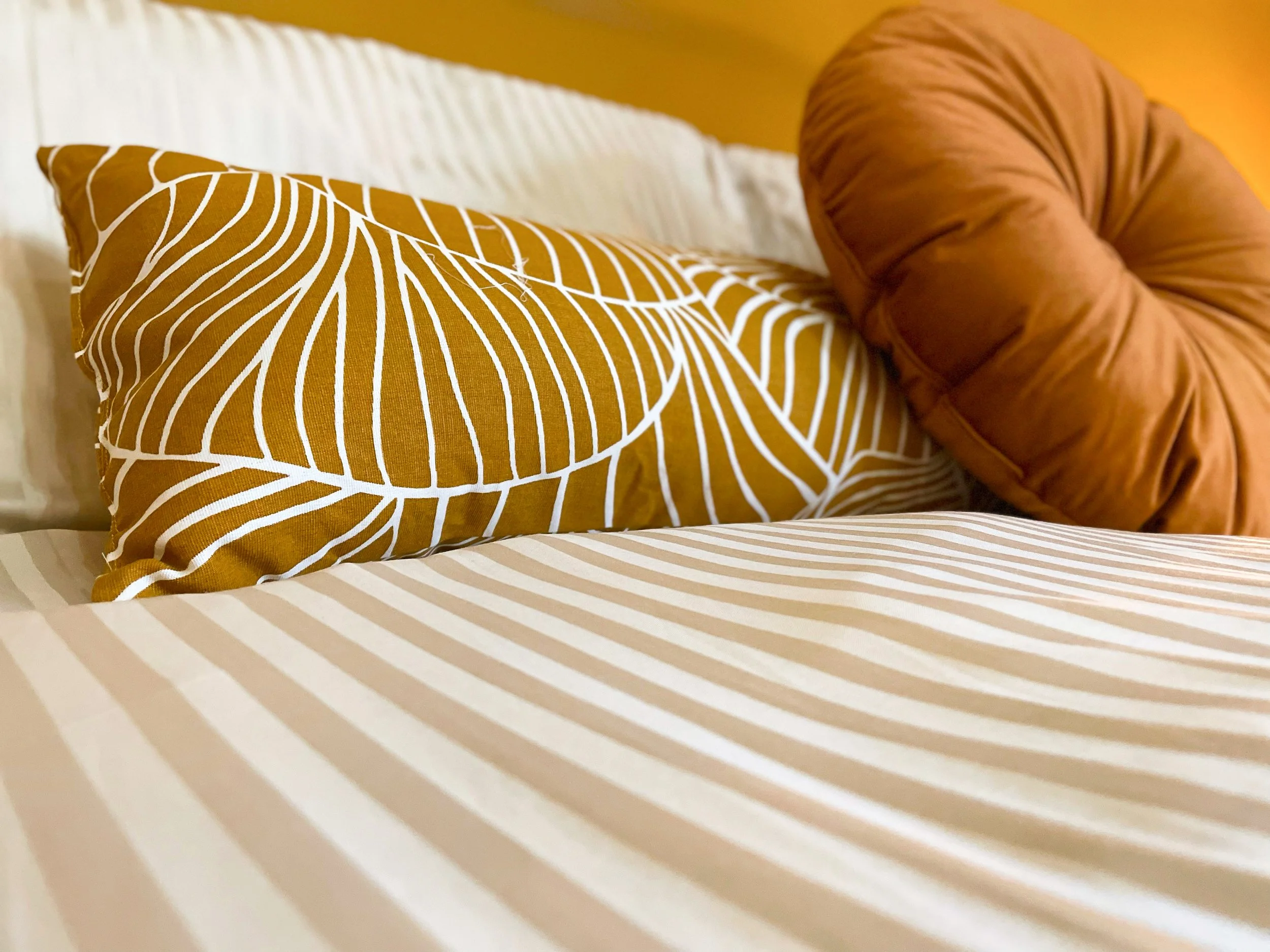 Cuscini decorativi su un letto con copriletto a righe beige e bianche.