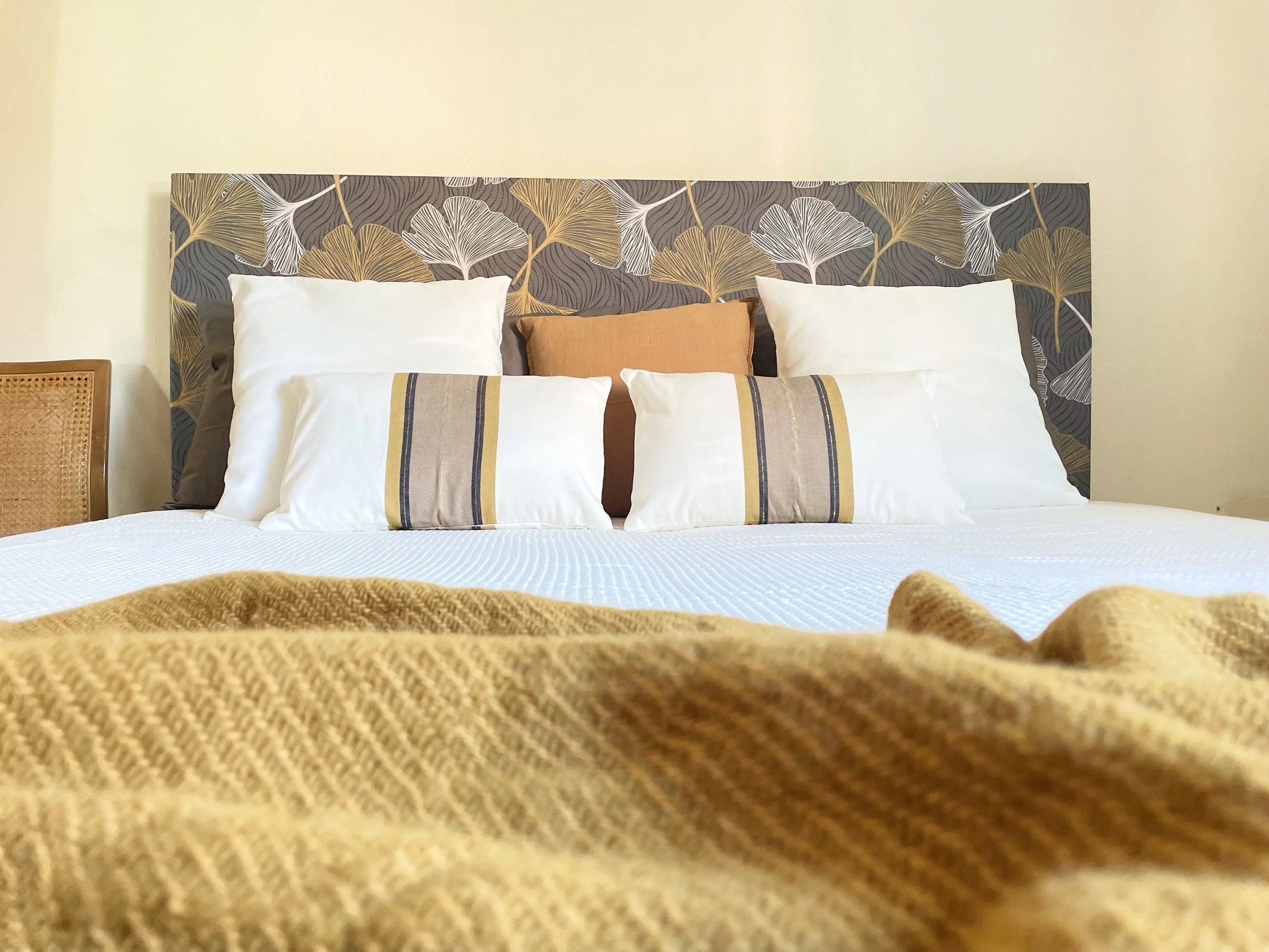 Letto matrimoniale con testiera decorata e coperte in tonalità neutre. Ci sono diversi cuscini bianchi e decorativi con motivi geometrici e a righe. L'atmosfera è accogliente e moderna.
