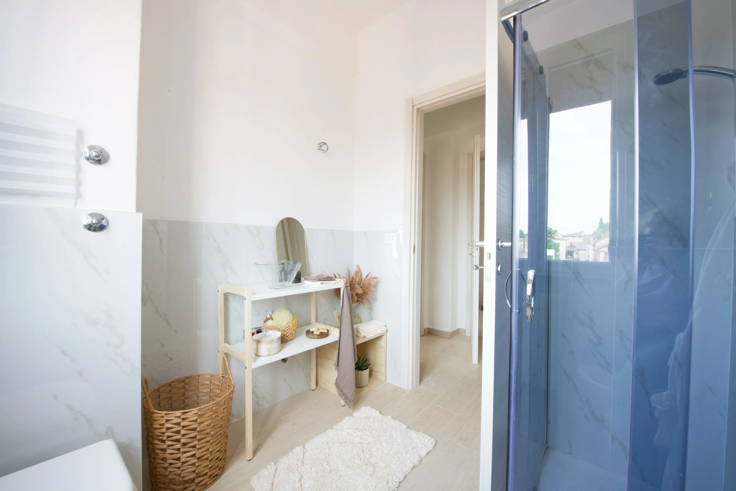 Bagno moderno con doccia in vetro, mensola con specchio, cestino intrecciato e decorazioni.