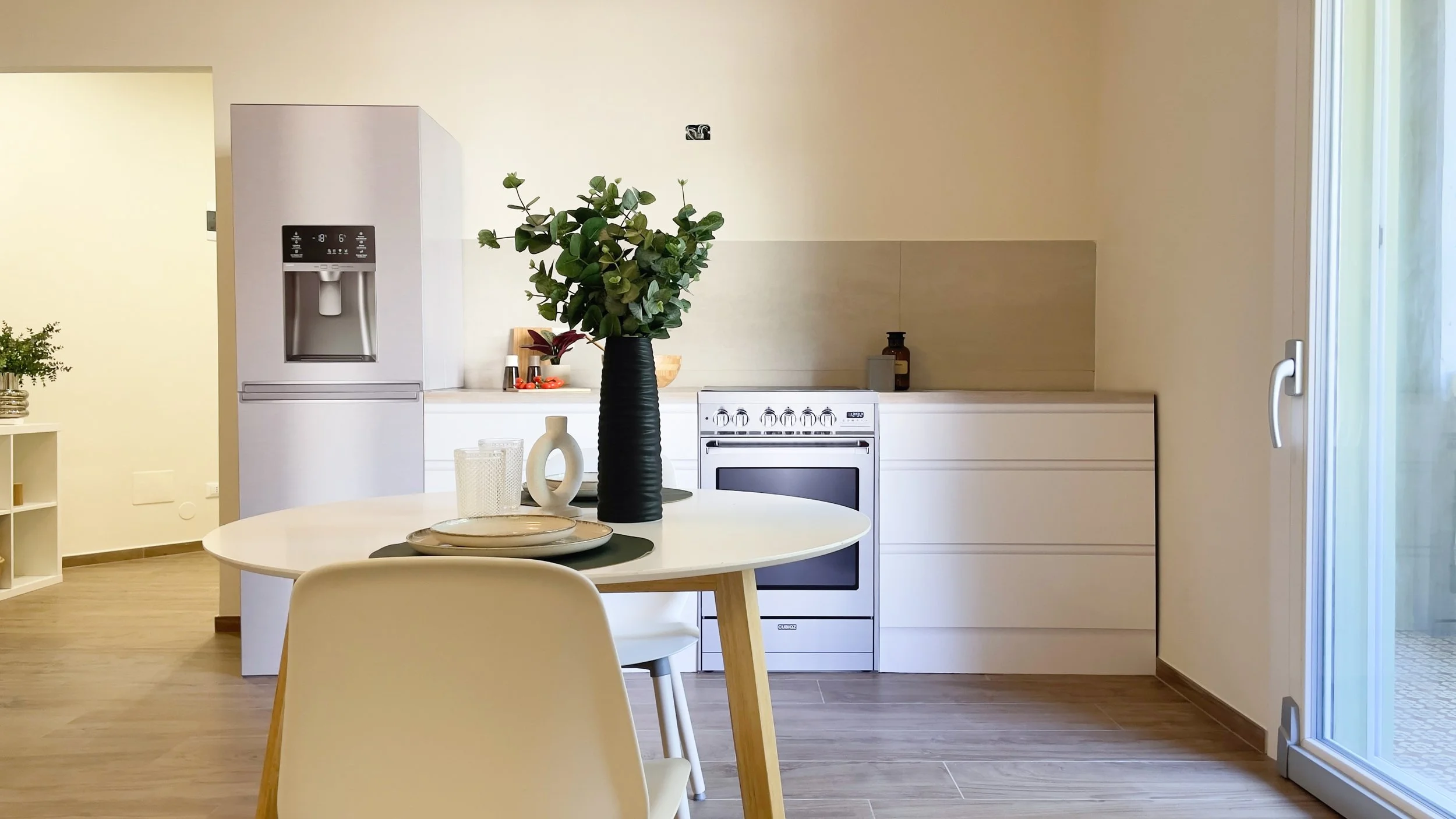 Cucina moderna con frigorifero, tavolo rotondo con sedie, e piante decorative.