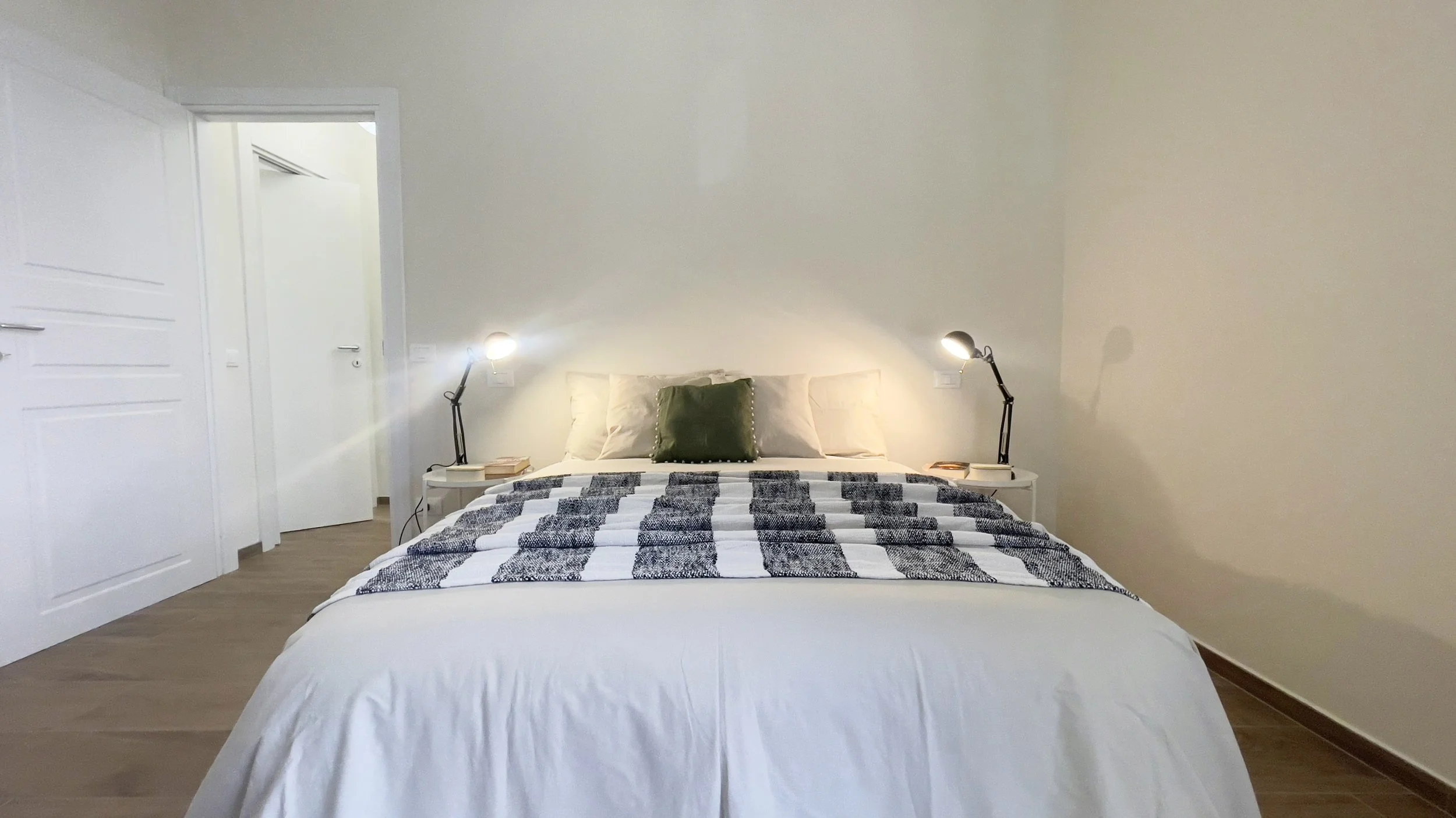 Camera da letto minimalista con letto matrimoniale, cuscini, coperta a strisce, lampade da lettura e comodini.