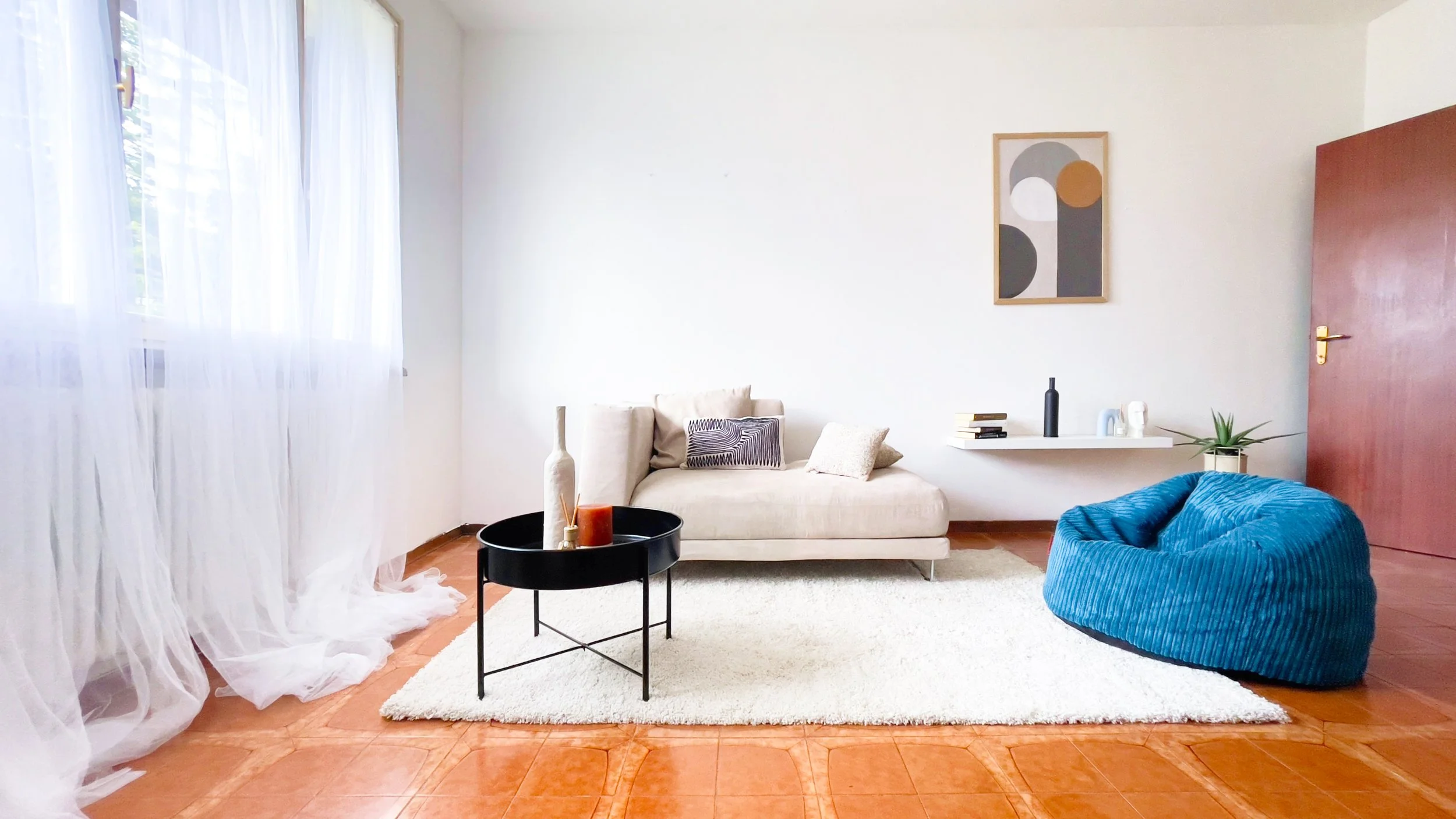 Soggiorno moderno con divano beige, pouf blu, tavolino nero e decorazioni minimaliste.