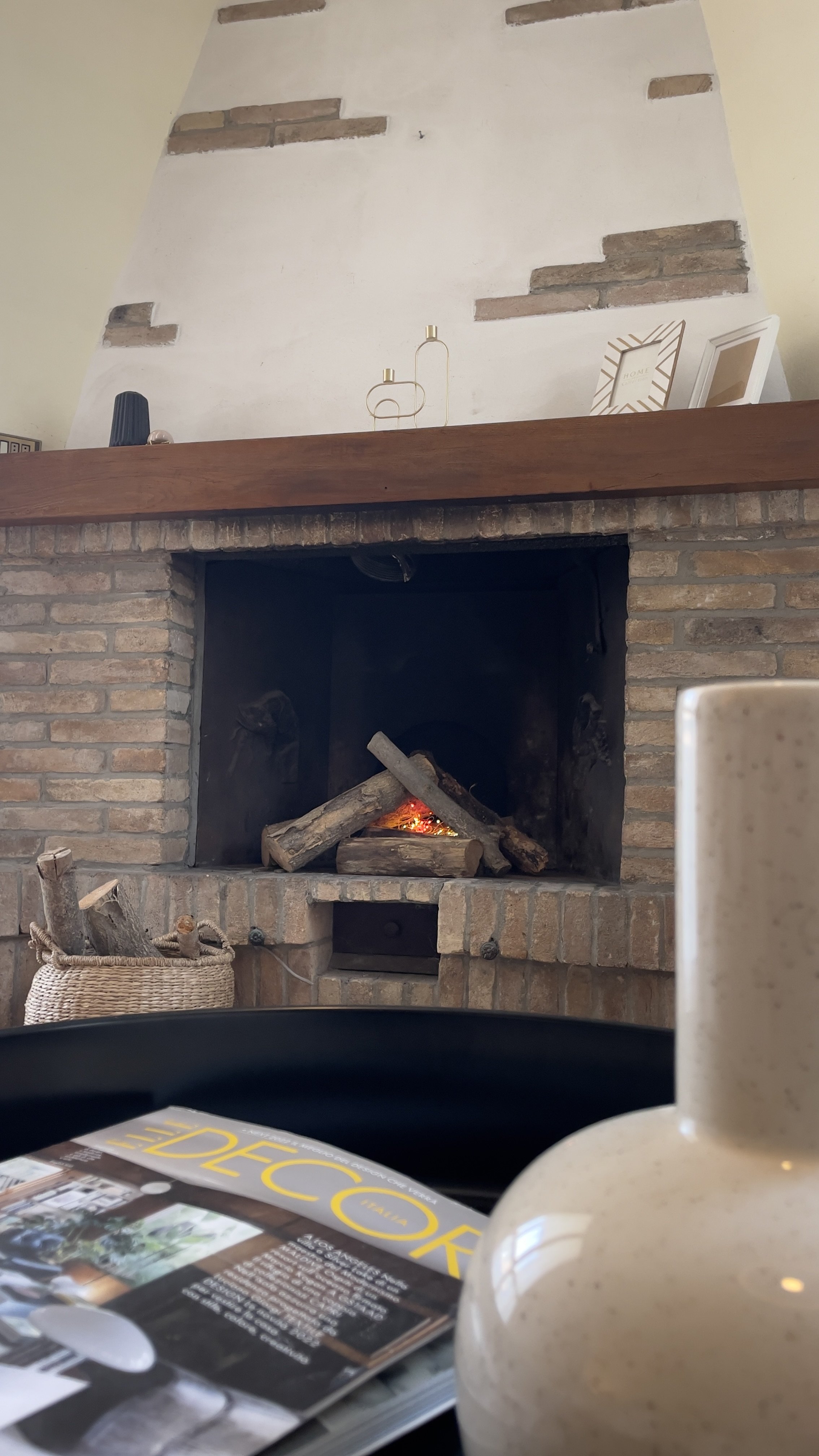 Camino acceso con legna, vaso decorativo, e rivista su un tavolo.