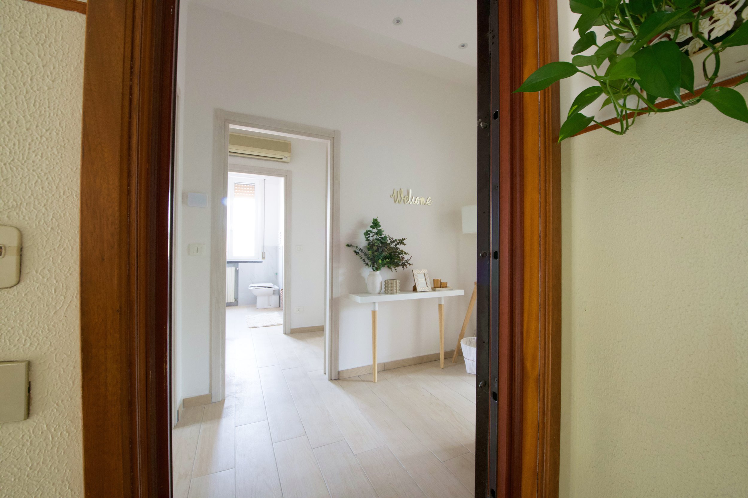 Ingresso di una casa moderna con pareti bianche e un tavolino con decorazioni floreali, vista sul bagno in fondo.
