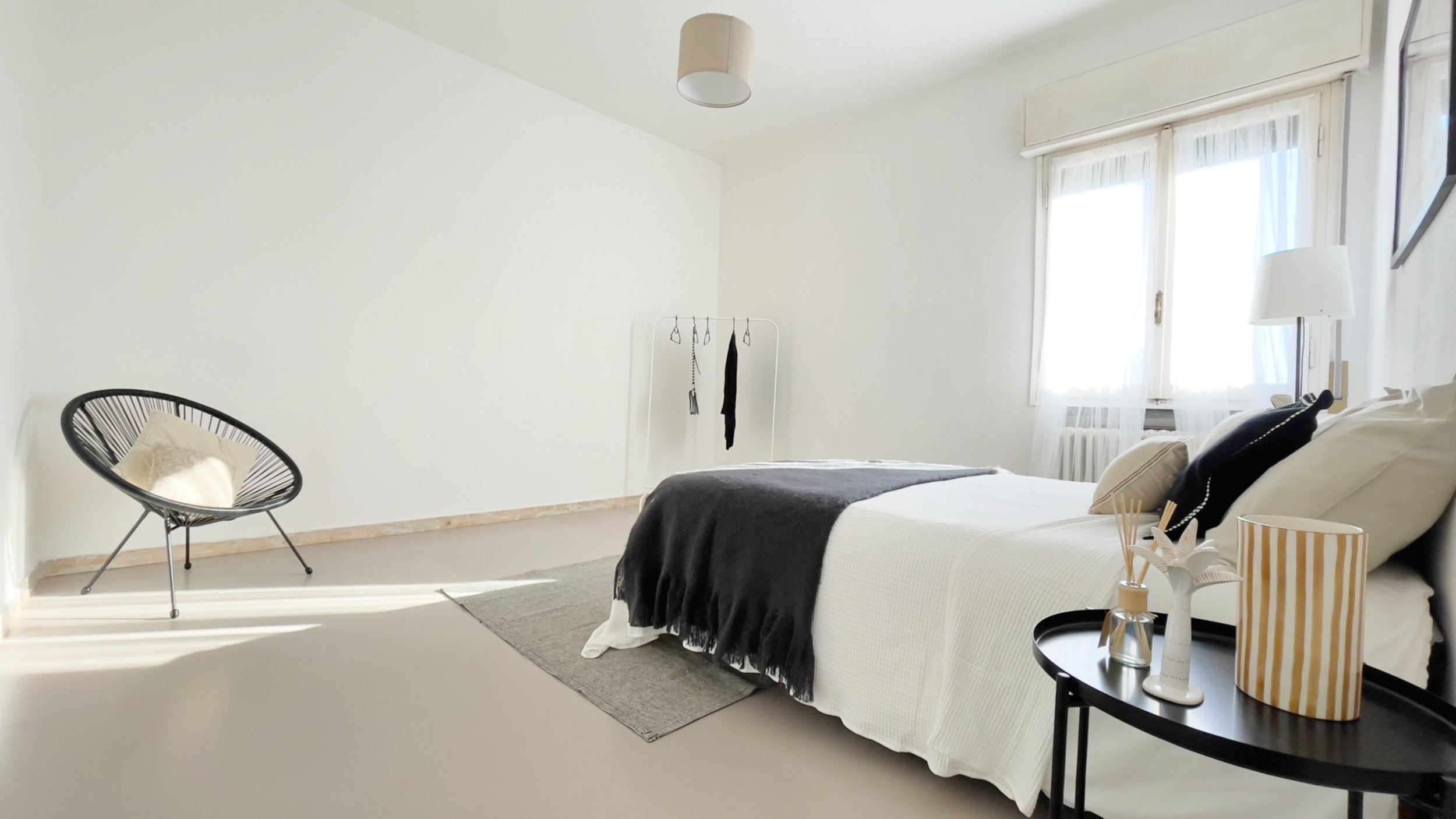 Camera da letto moderna con letto matrimoniale, coperta nera, finestra luminosa, sedia nera e tavolino con decorazioni.