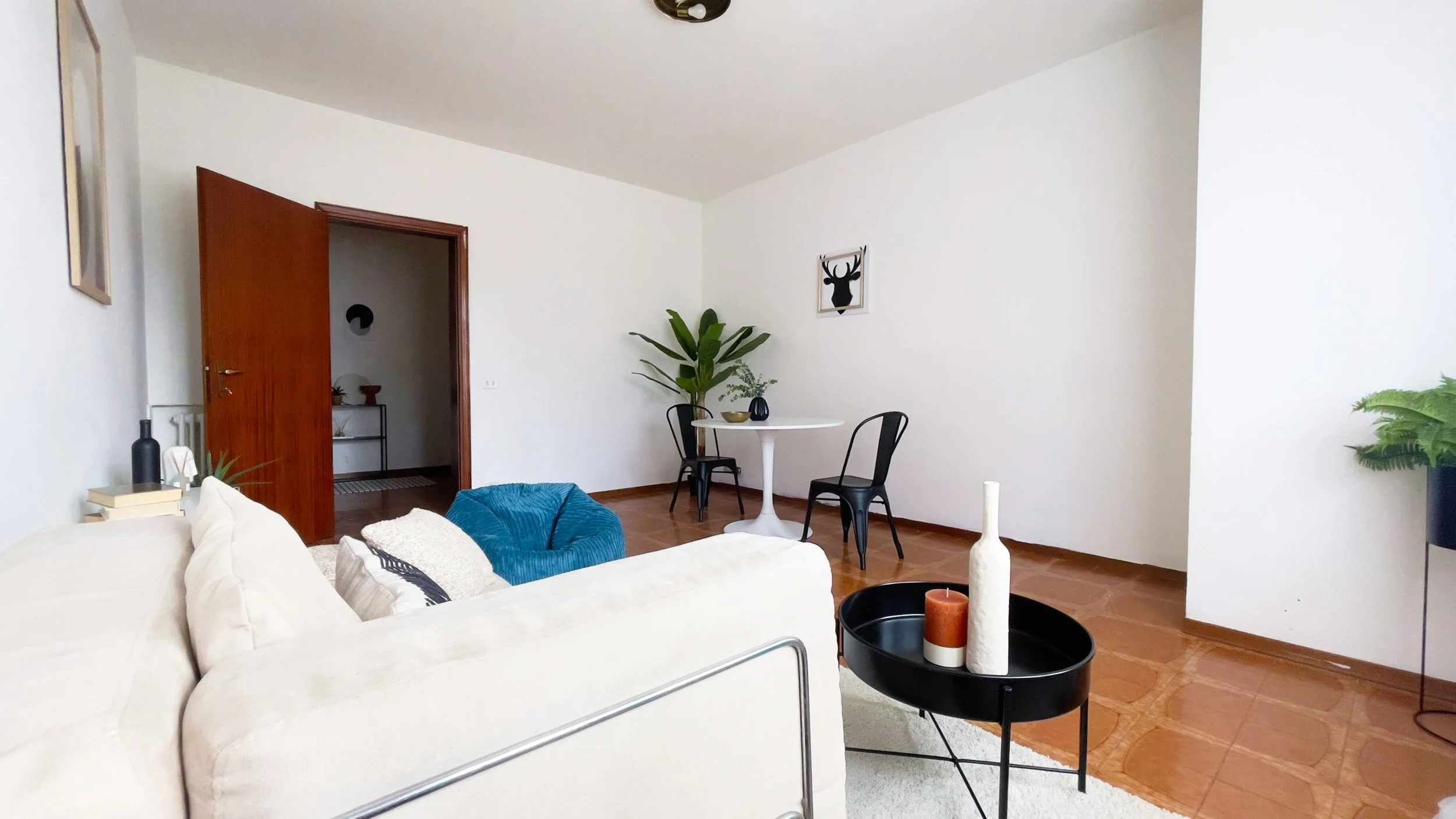 Soggiorno moderno con divano beige, tavolino nero, pianta verde, tavolo bianco e due sedie nere, porta aperta, decorazioni minimaliste.