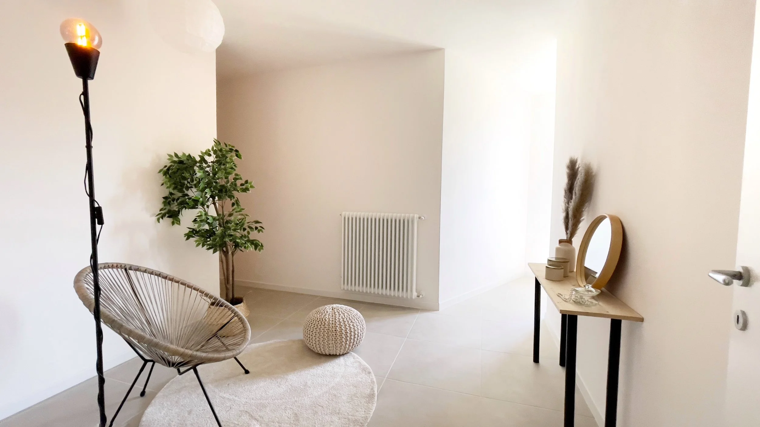 Interno di una stanza minimalista con una sedia di design, lampada a piantana, tappeto rotondo, pianta verde, pouf lavorato a maglia, console con specchio e vasi decorativi.