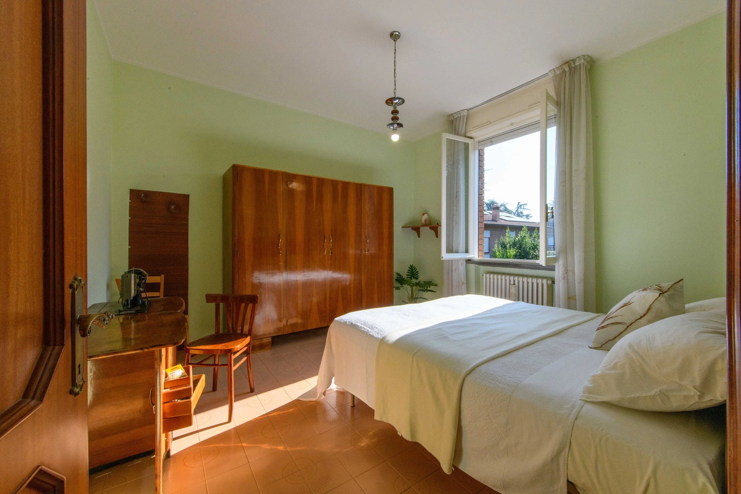 Camera da letto luminosa con pareti verdi, letto matrimoniale, armadio in legno, scrivania con sedia e finestra aperta.