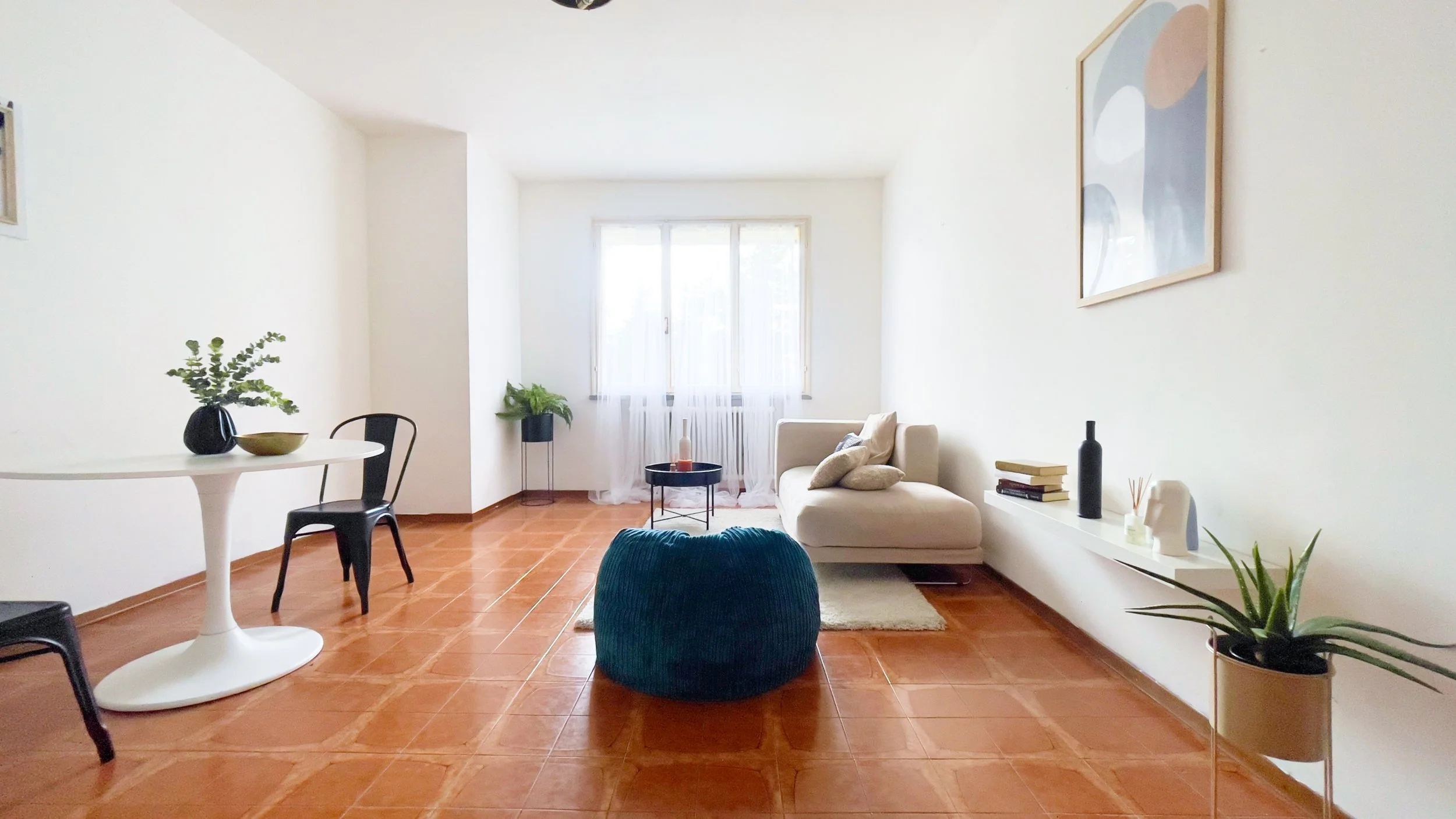 Soggiorno moderno con pavimento in piastrelle arancioni, divano bianco, tavolino bianco con sedie nere, pianta verde, quadri alle pareti e decorazioni minimaliste.