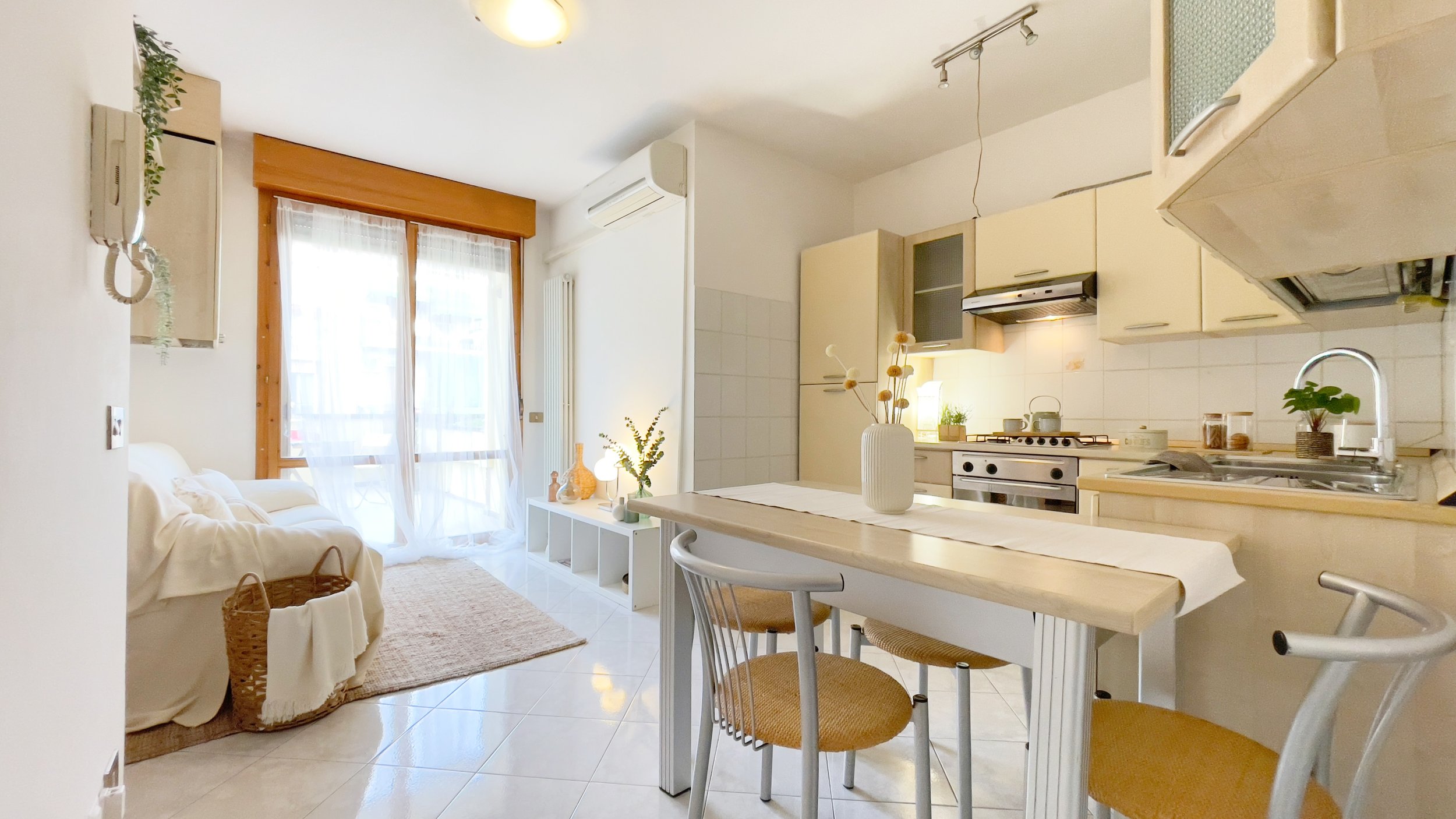 Cucina e salotto moderni, luminosi, con tavolo e sedie, divano bianco, cucina attrezzata e finestre ampie.