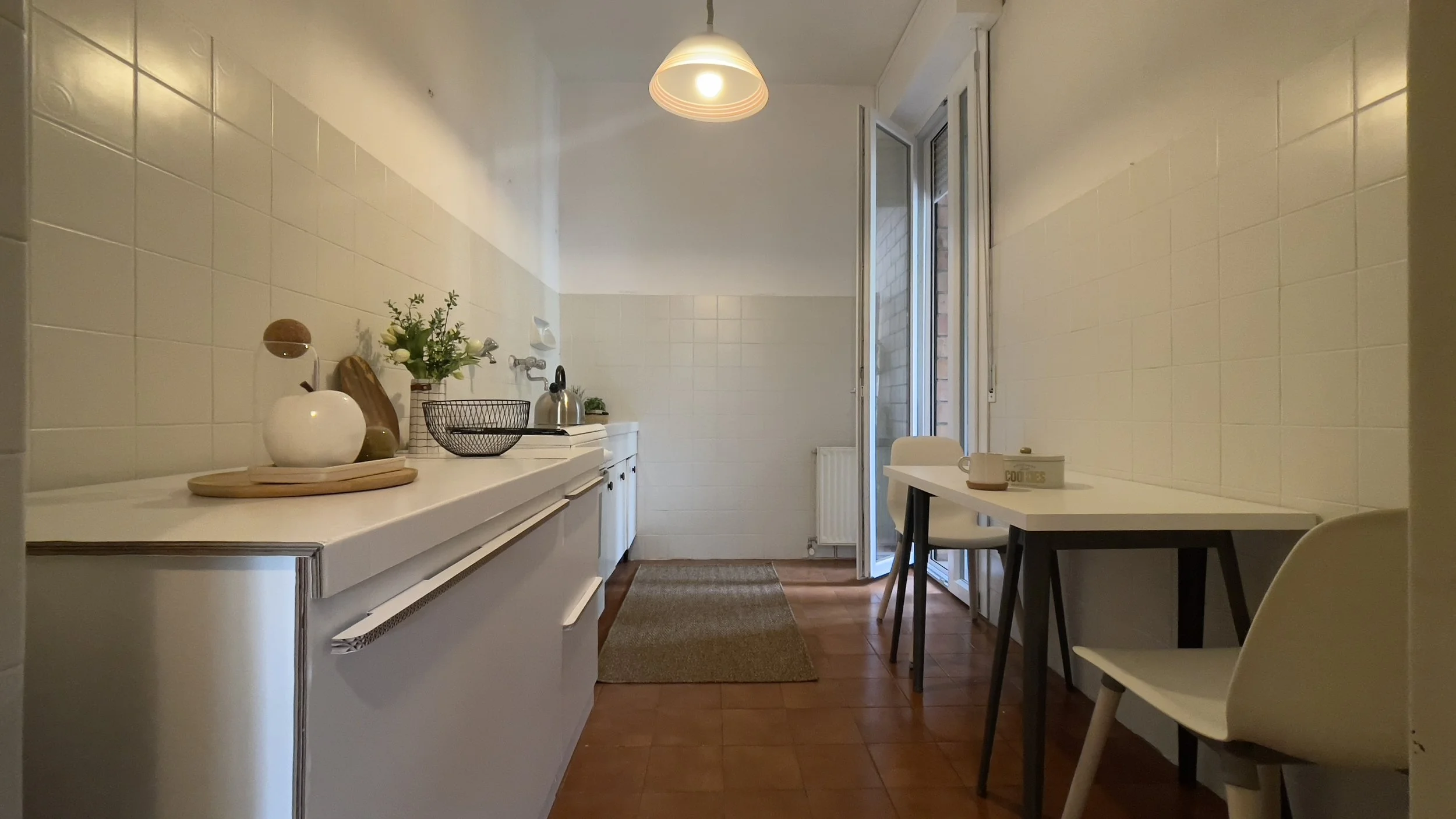 Cucina con arredamento minimalista, tavolo e sedie bianche, e oggetti decorativi sul bancone.