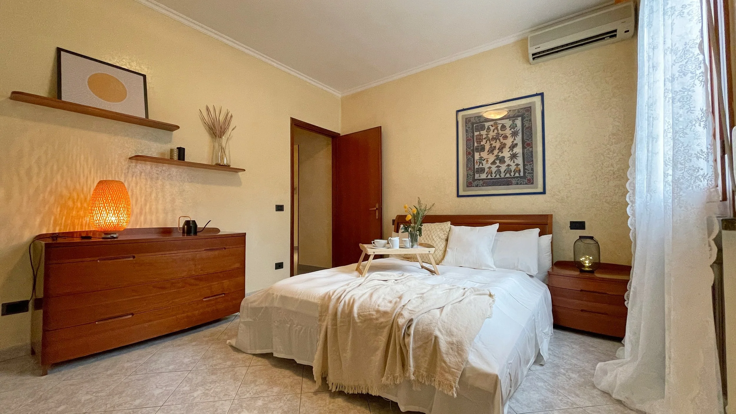 Camera da letto con letto matrimoniale, comodino, lampada arancione, aria condizionata, e decorazioni sulla parete.
