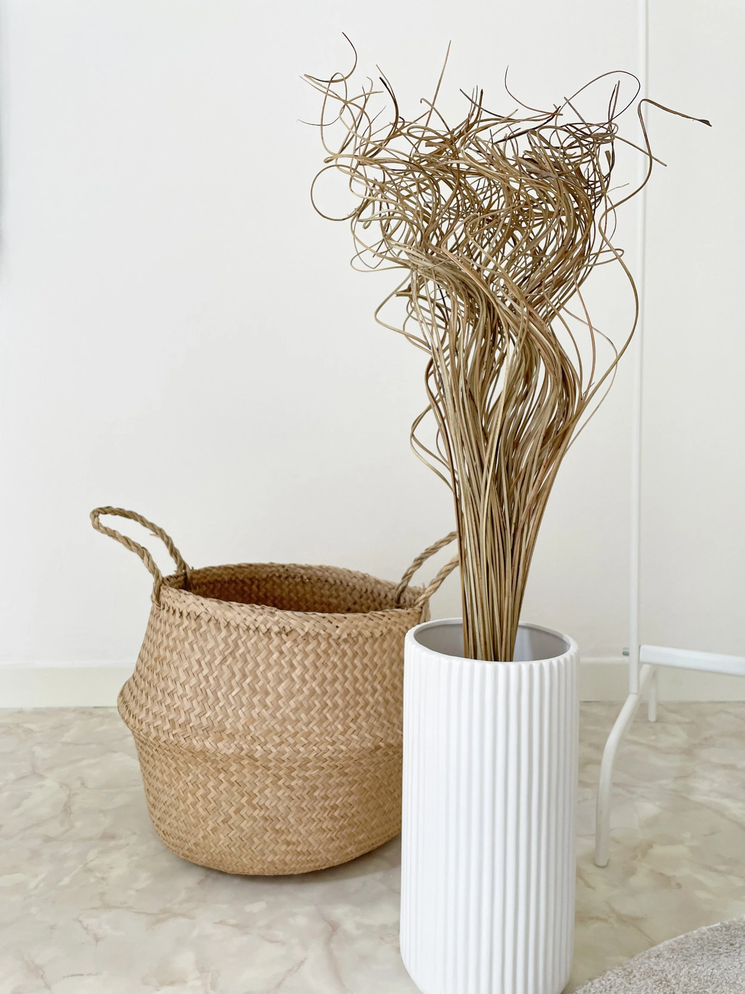 Cesto di vimini e vaso bianco con rami decorativi su pavimento chiaro