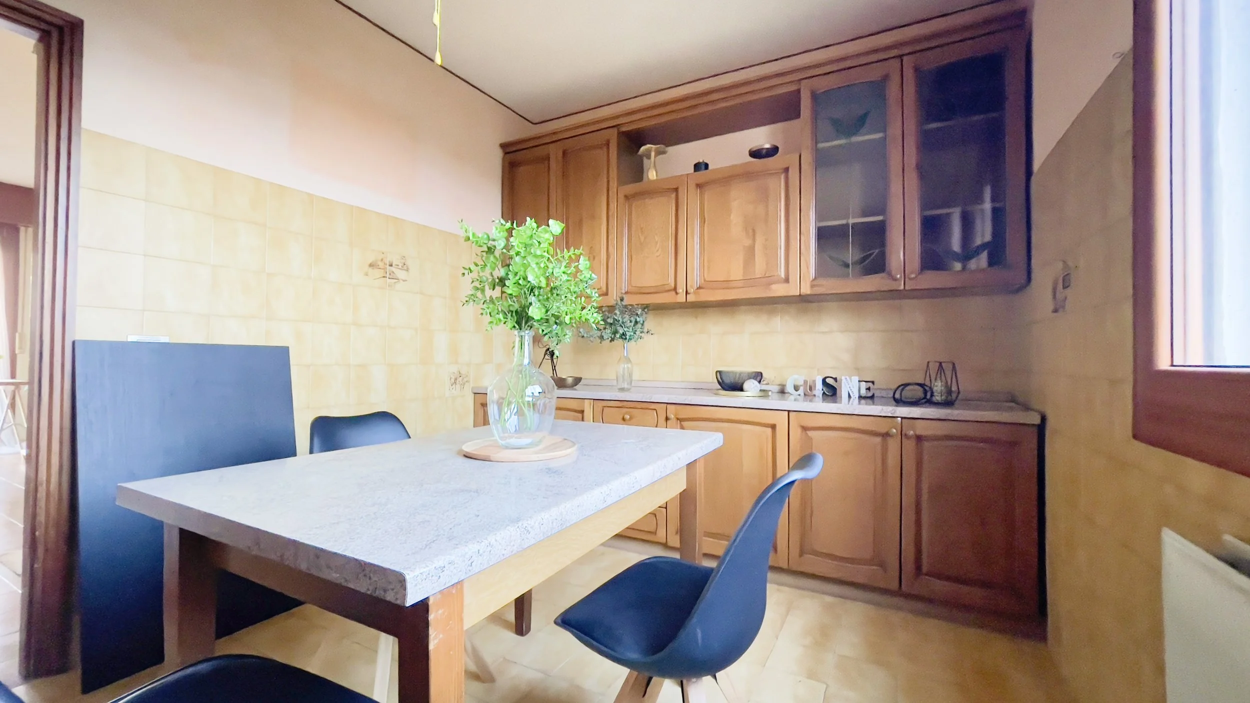 Cucina con tavolo in legno grigio, sedie nere, armadietti in legno e decorazioni.