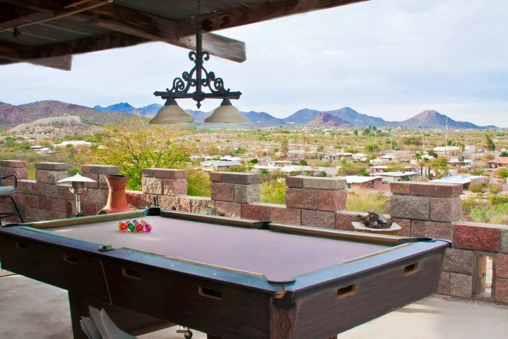 Pool table on a patio overlooking a desert landscape with mountains in the distance.