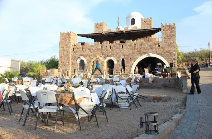 Outdoor dining area with multiple round tables and white chairs set up in front of a church-like building made of brick with a white dome on top, during daytime.