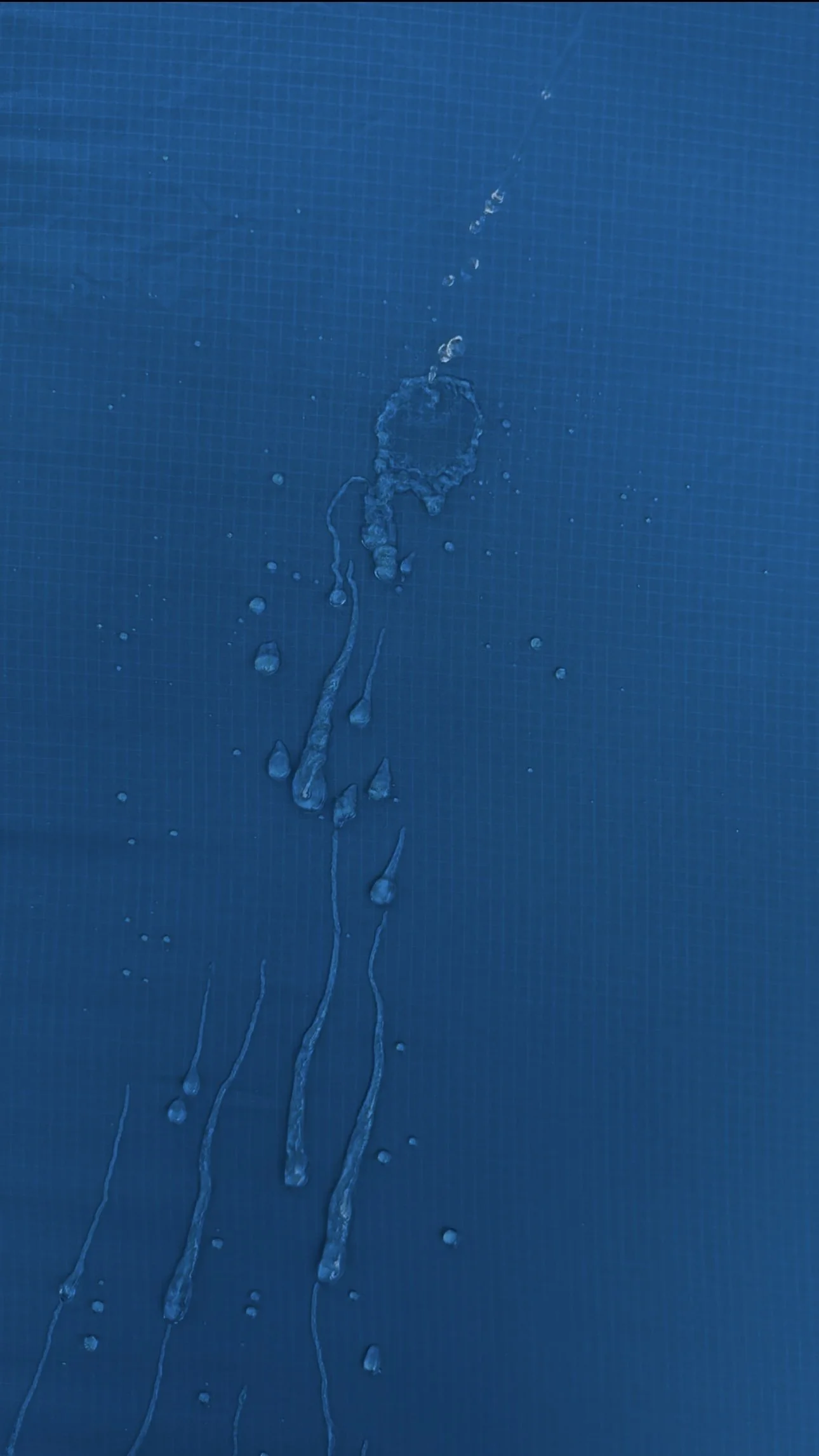 Water droplets and streaks on a textured blue surface.