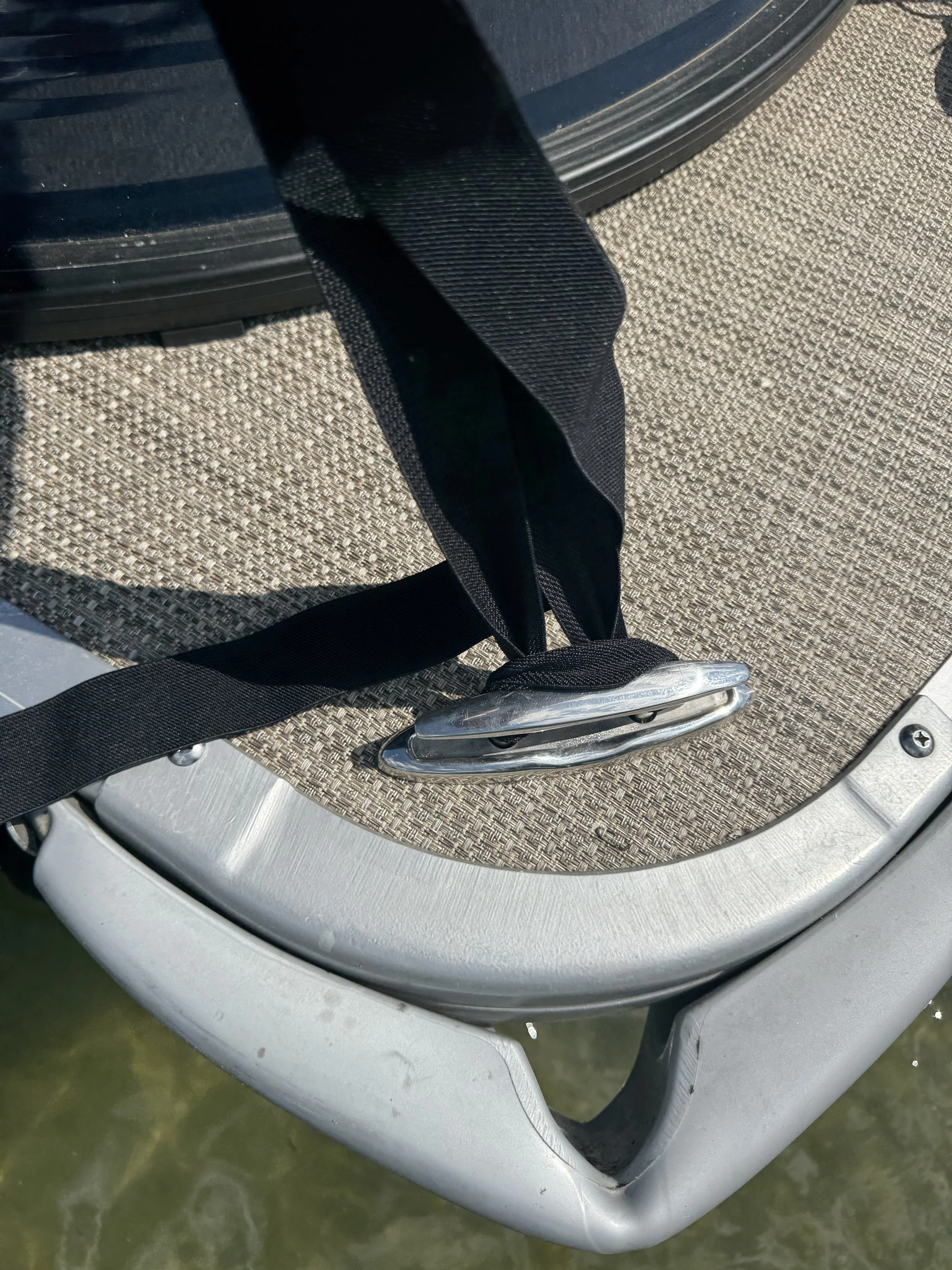 Close-up of a boat seat with a black strap and a metal hook, with water underneath.