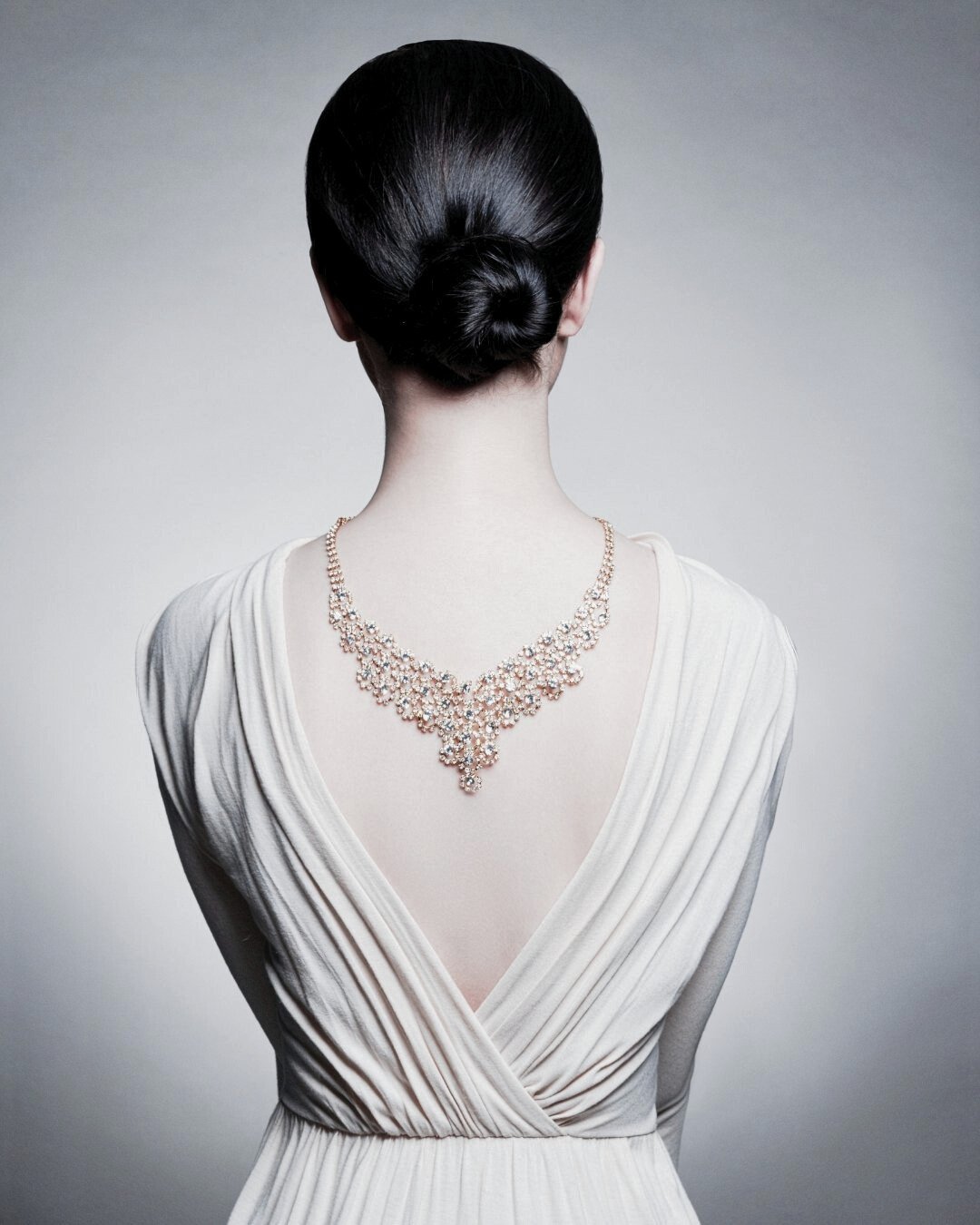 Back view of an elegant woman in a white gown wearing a diamond necklace draped down her back, symbolising personal style and refined elegance