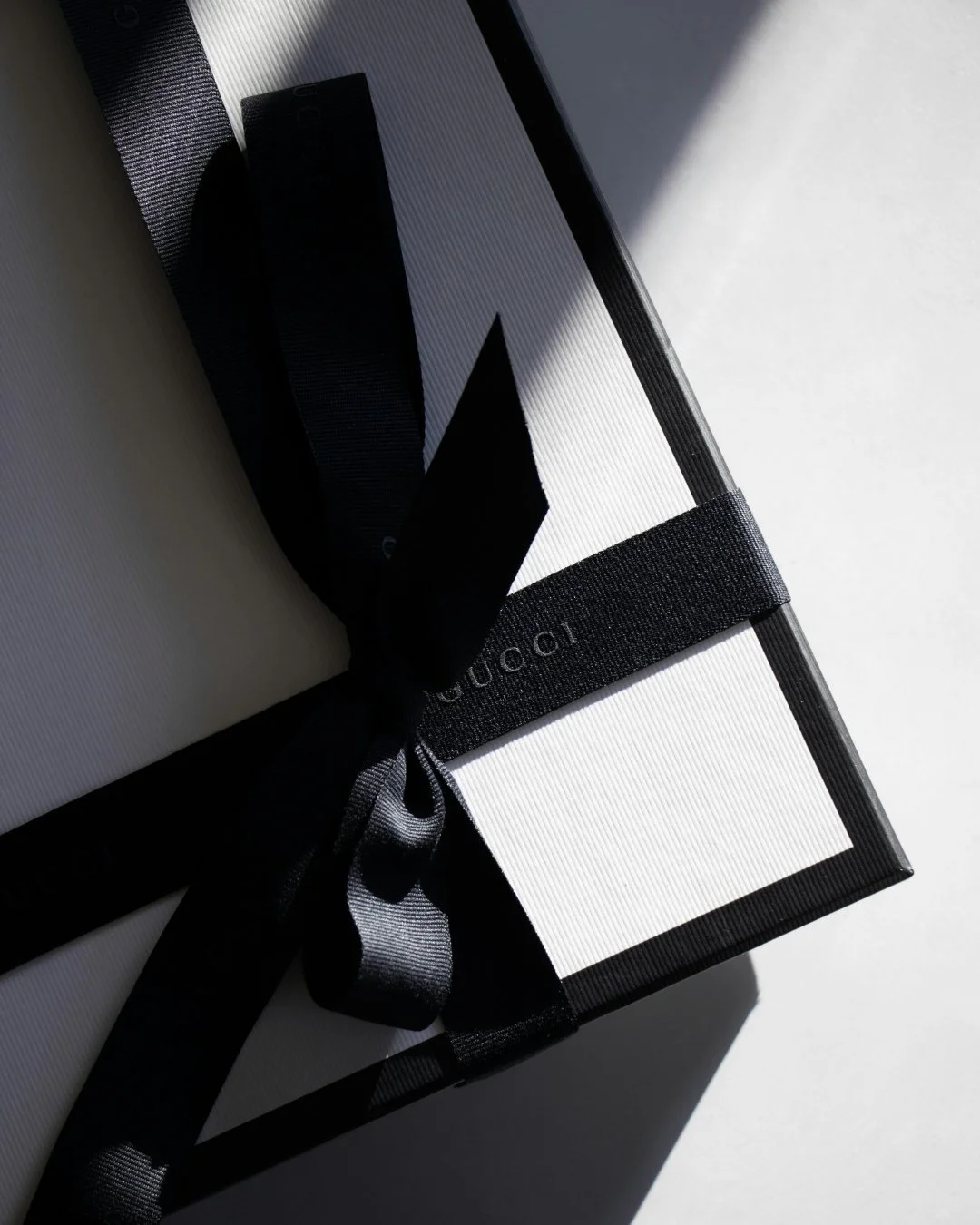 Elegant black and white image of a Gucci gift box wrapped with a black silk ribbon, symbolising bespoke gift selection and refined presentation