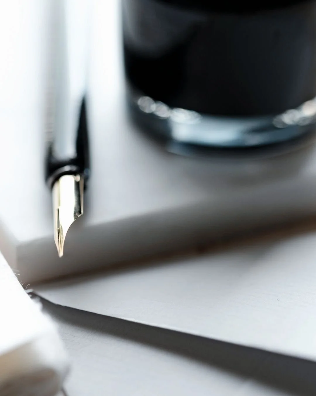 Close-up of a fountain pen tip resting on white papers next to a bottle of ink, evoking refined writing and luxury correspondence