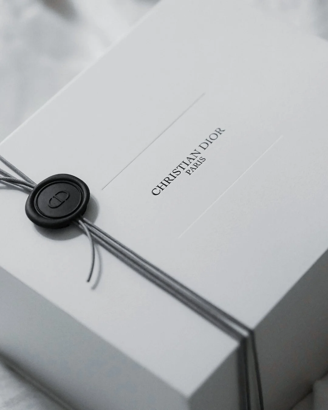 Unopened white Dior package sealed with black wax, representing the art of shopping and refined anticipation