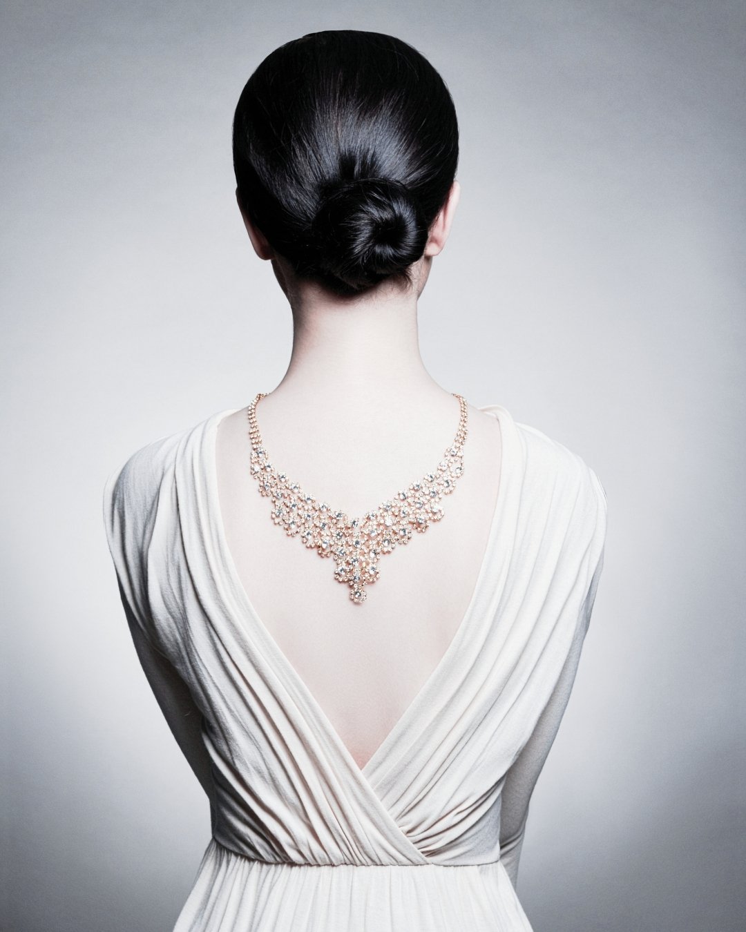 Back view of an elegant woman in a white gown wearing a diamond necklace draped down her back, symbolising personal style and refined elegance