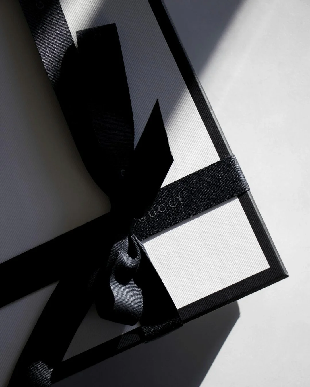 Elegant black and white image of a Gucci gift box wrapped with a black silk ribbon, symbolising bespoke gift selection and refined presentation