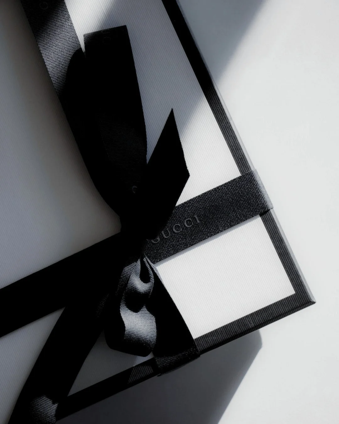 Elegant black and white image of a Gucci gift box wrapped with a black silk ribbon, symbolising bespoke gift selection and refined presentation
