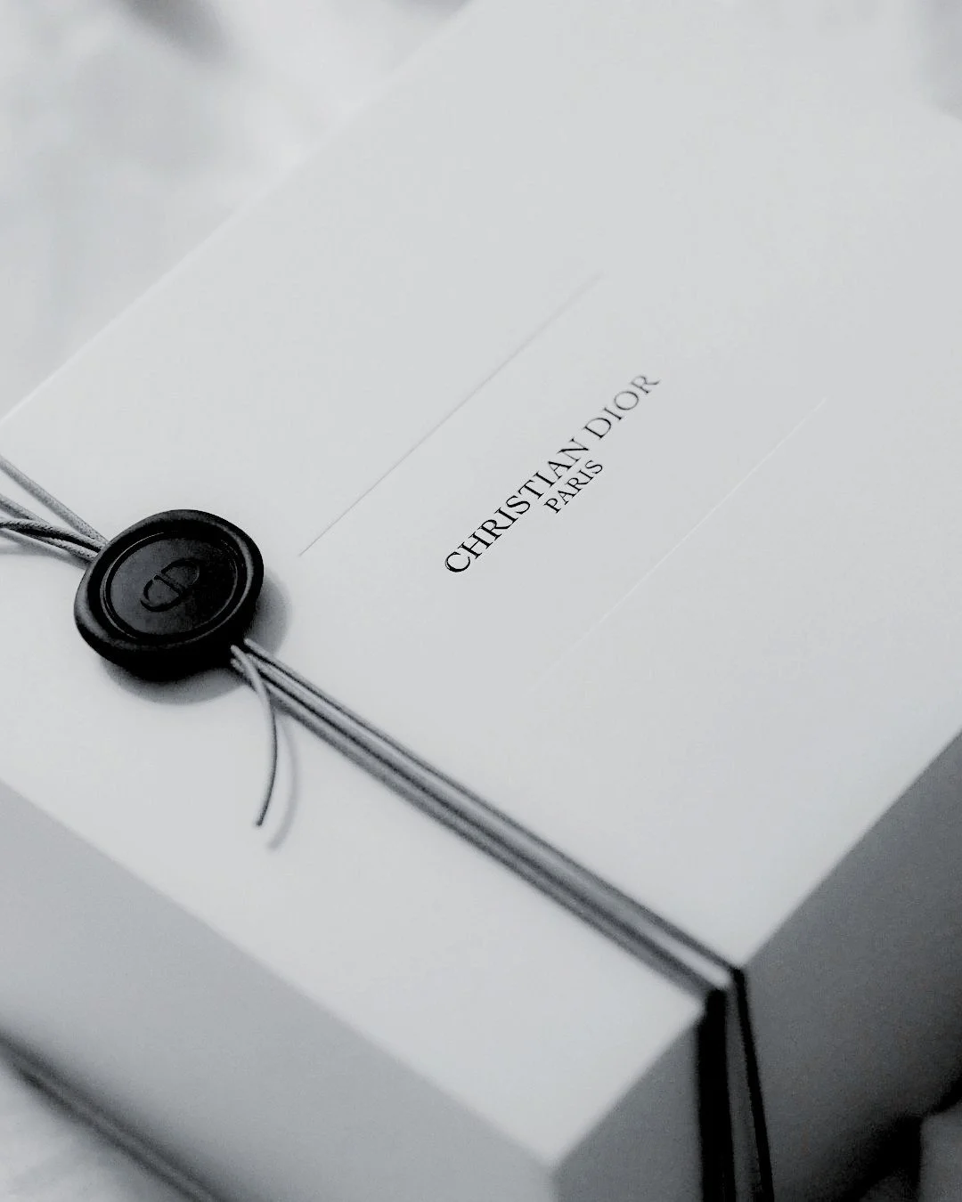 Unopened white Dior package sealed with black wax, representing the art of shopping and refined anticipation