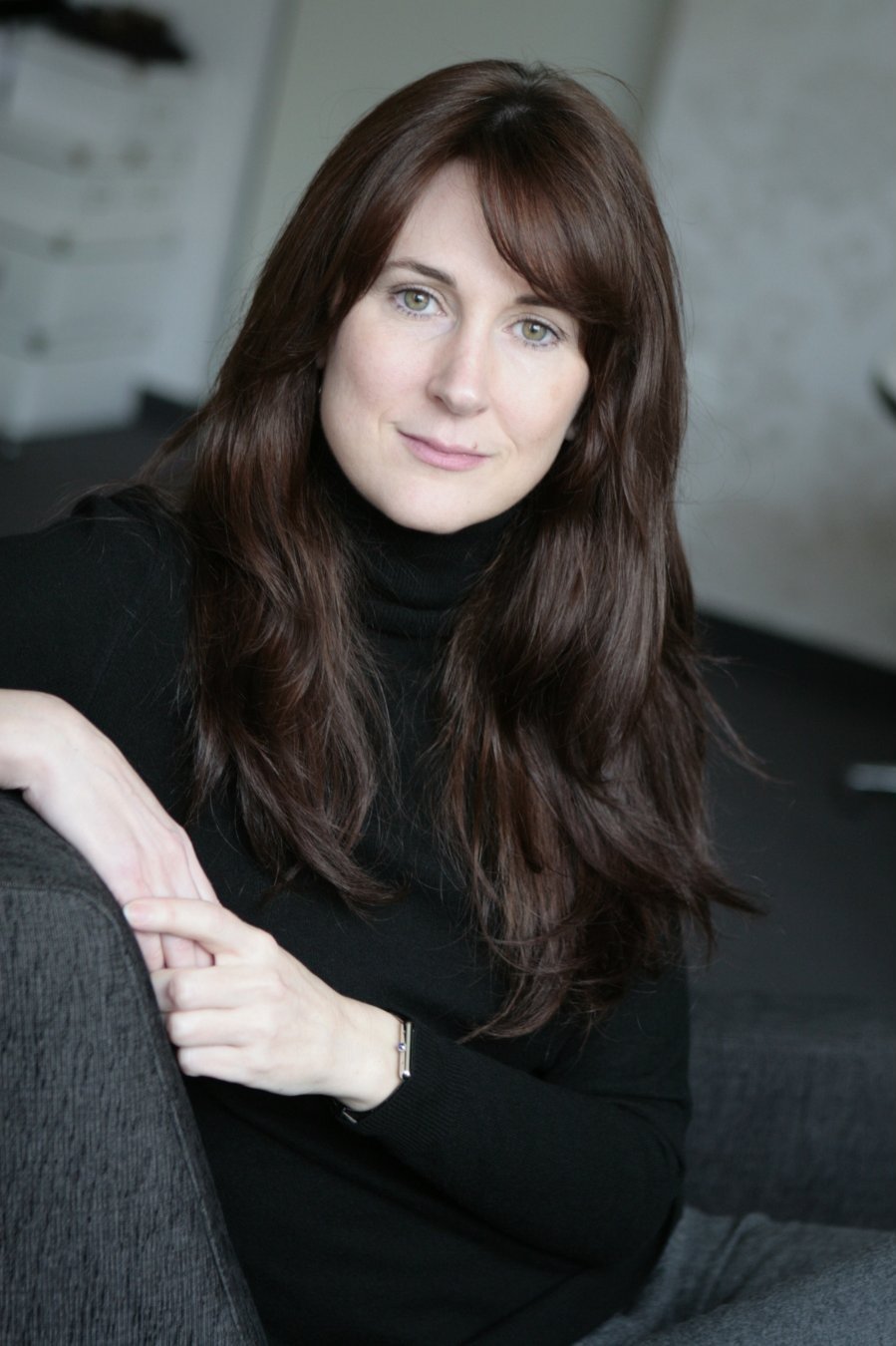 Zita Pavláth seated on a grey chair, showcasing elegance and poise, representing luxury fashion consultancy