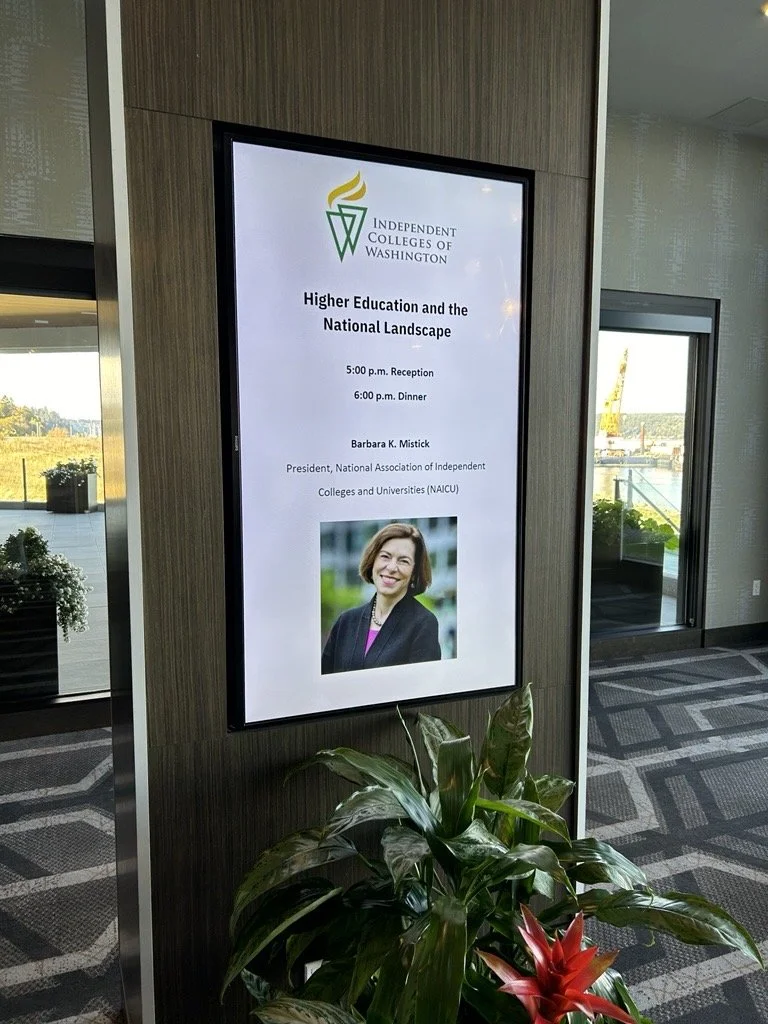 Digital display at a conference for the Independent Colleges of Washington, announcing a session on 'Higher Education and the National Landscape' featuring Barbara K. Mistick, with reception at 5:00 p.m. and dinner at 6:00 p.m., and including a photo of Barbara K. Mistick.